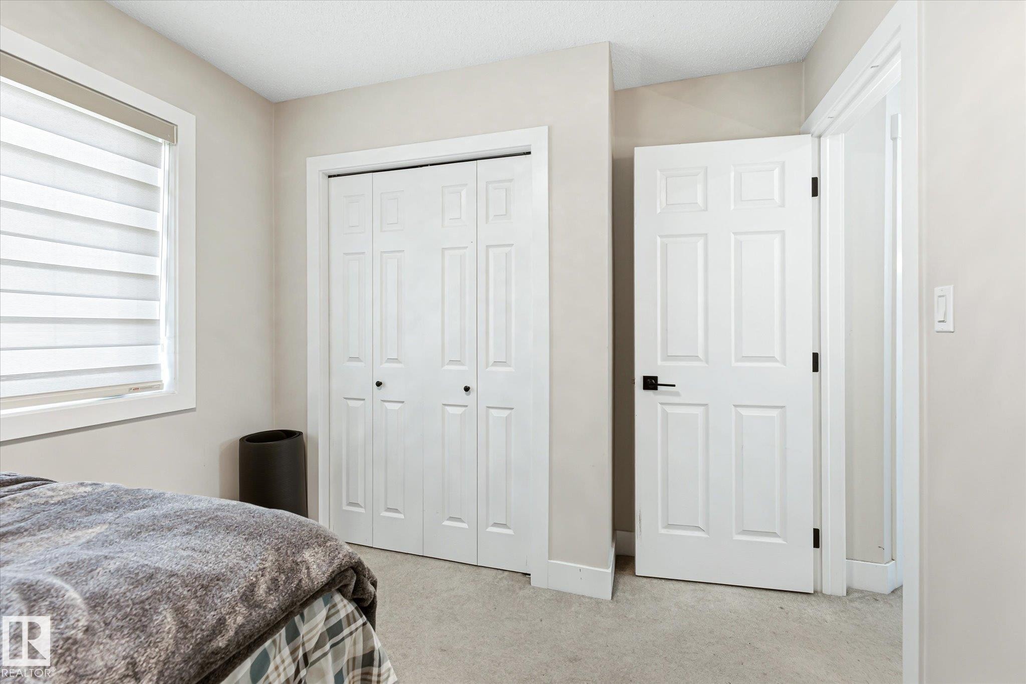 Bedroom with neutral wall tones, light-toned carpet flooring, and a window with horizontal blinds - 4317 152 Avenue Nw, Edmonton, AB - Indoor Photo Showing Bedroom