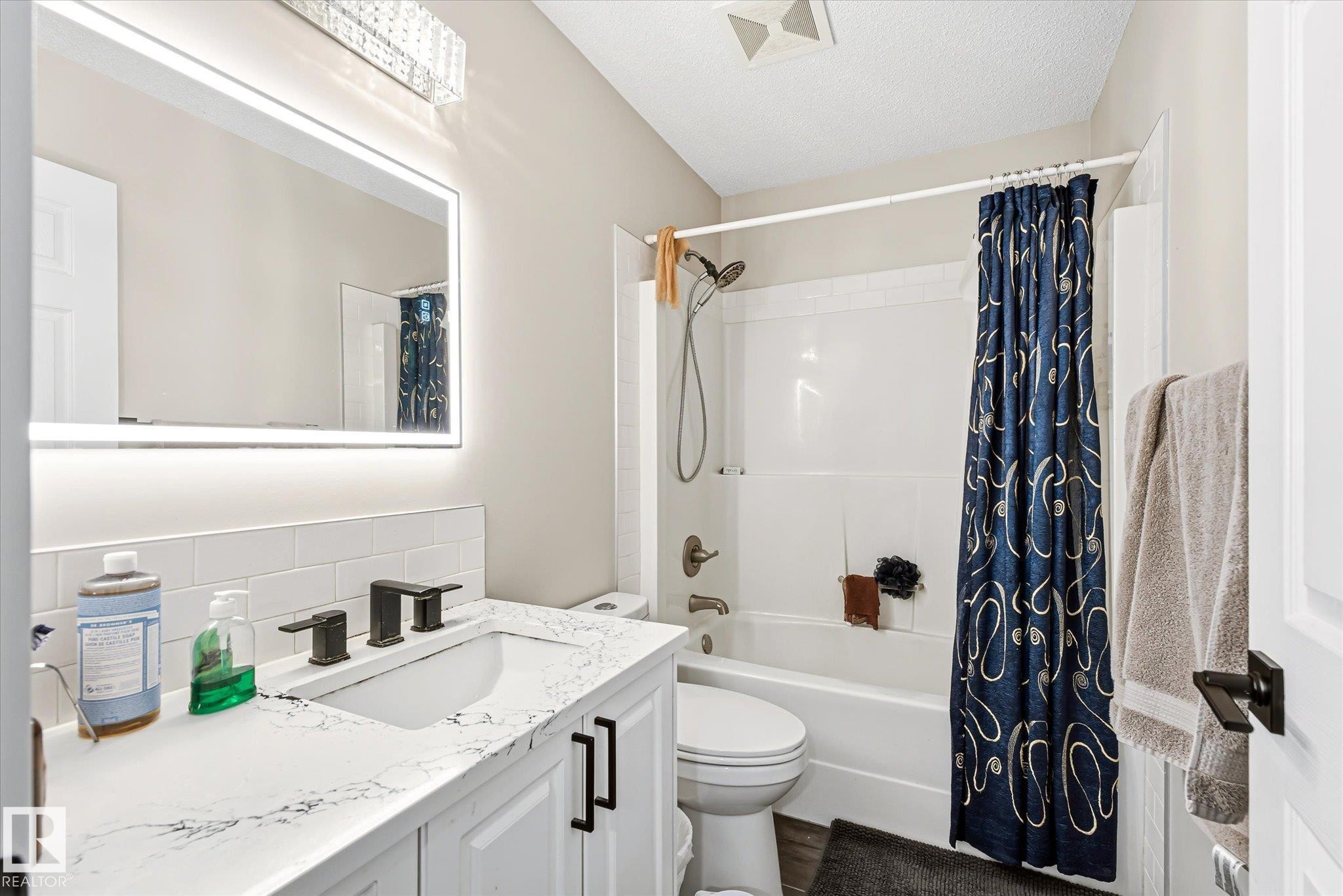 Bathroom featuring a white vanity with a solid surface countertop, an undermount sink, and matte black fixtures - 4317 152 Avenue Nw, Edmonton, AB - Indoor Photo Showing Bathroom