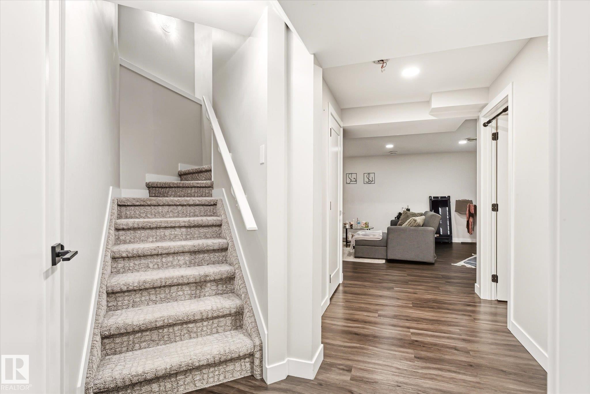 Carpeted staircase with white handrail and trim, featuring a wood-finish flooring hallway and recessed lighting - 4317 152 Avenue Nw, Edmonton, AB - Indoor Photo Showing Other Room