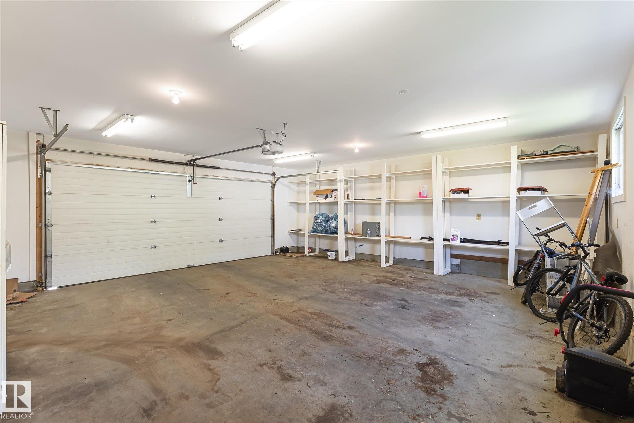 Spacious garage featuring a white sectional overhead door, concrete flooring, built-in shelving, recessed lighting, and fluorescent overhead lighting - 4317 152 Avenue Nw, Edmonton, AB - Indoor Photo Showing Garage