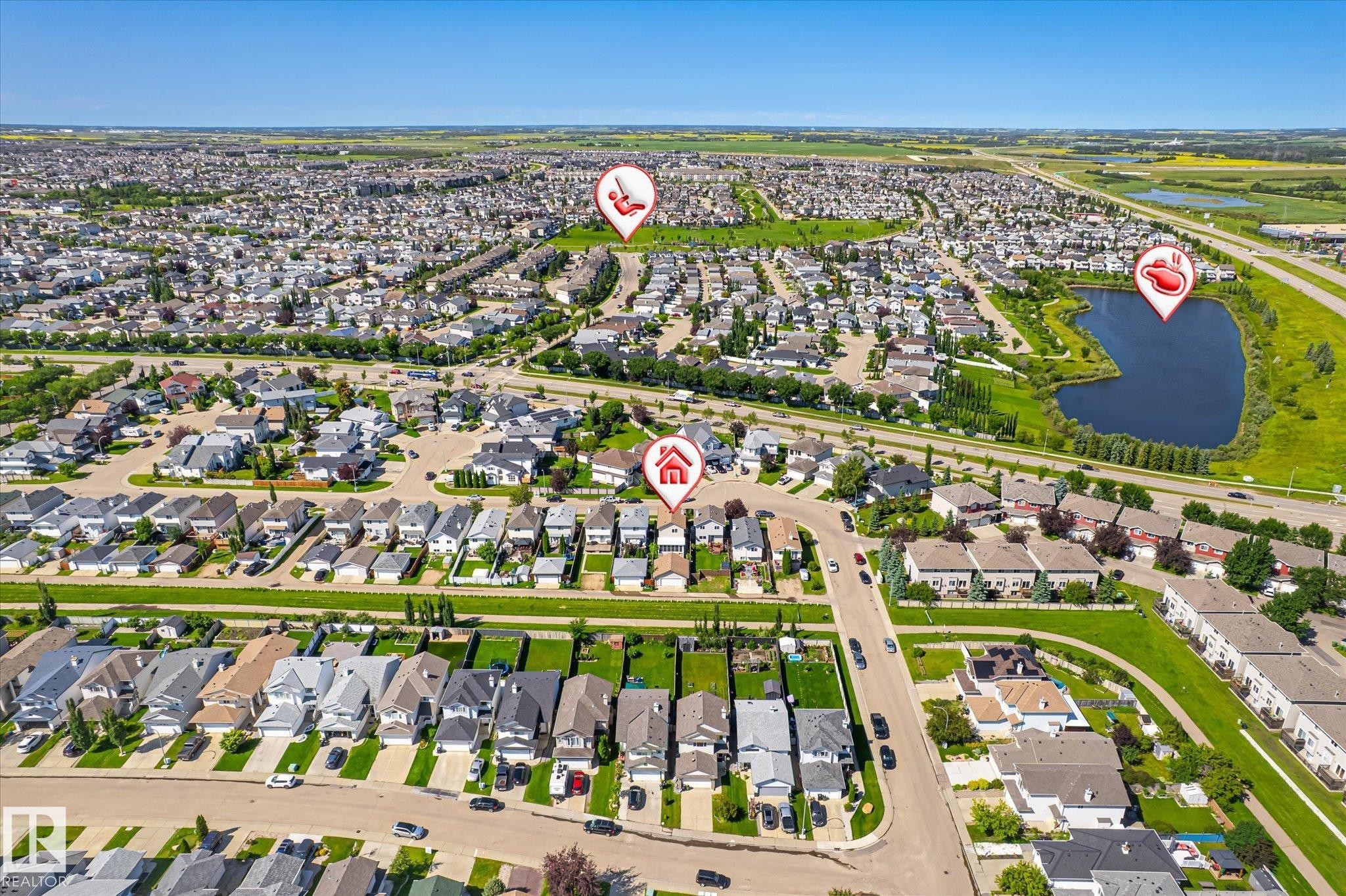 Expansive aerial perspective showcasing a residential development with numerous single-family homes and townhomes, a significant water feature, abundant green spaces, and surrounding infrastructure - 4317 152 Avenue Nw, Edmonton, AB - Outdoor With View