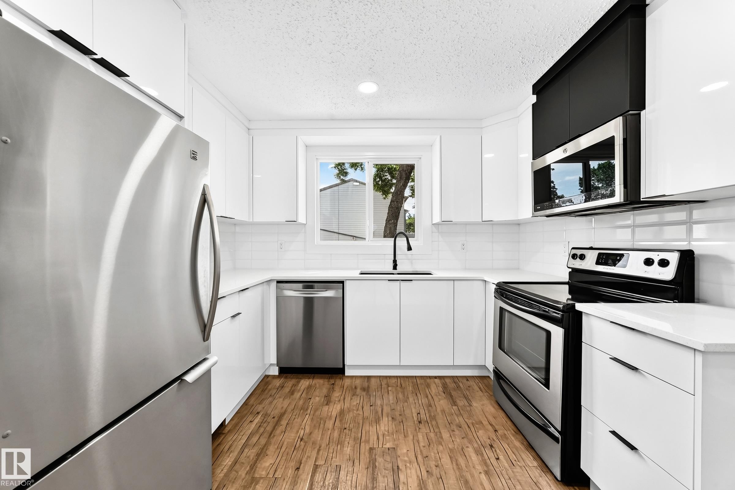 Modern kitchen featuring stainless steel appliances, white cabinetry, quartz countertops, white subway tile backsplash, and wood-finish flooring - 3119 144 Avenue Nw, Edmonton, AB - Indoor Photo Showing Kitchen With Upgraded Kitchen