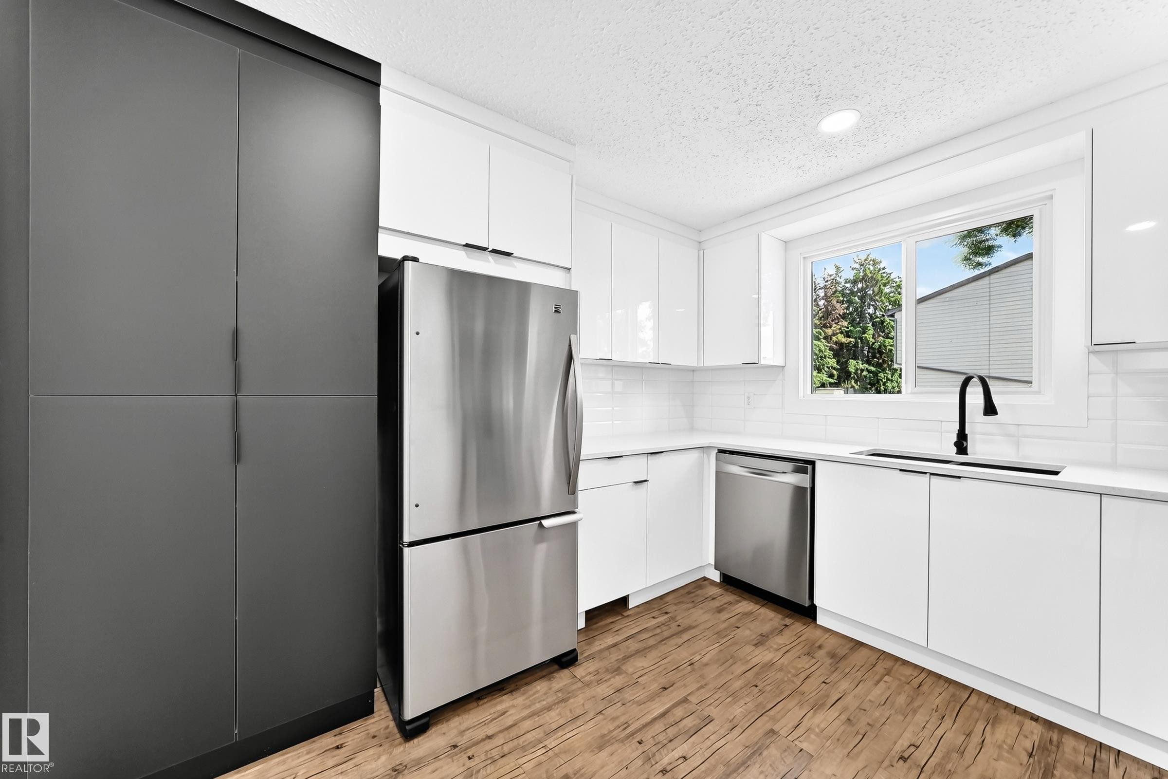 Modern kitchen featuring white cabinetry, stainless steel appliances, wood-finish flooring, white subway tile backsplash, and a black gooseneck faucet - 3119 144 Avenue Nw, Edmonton, AB - Indoor Photo Showing Kitchen