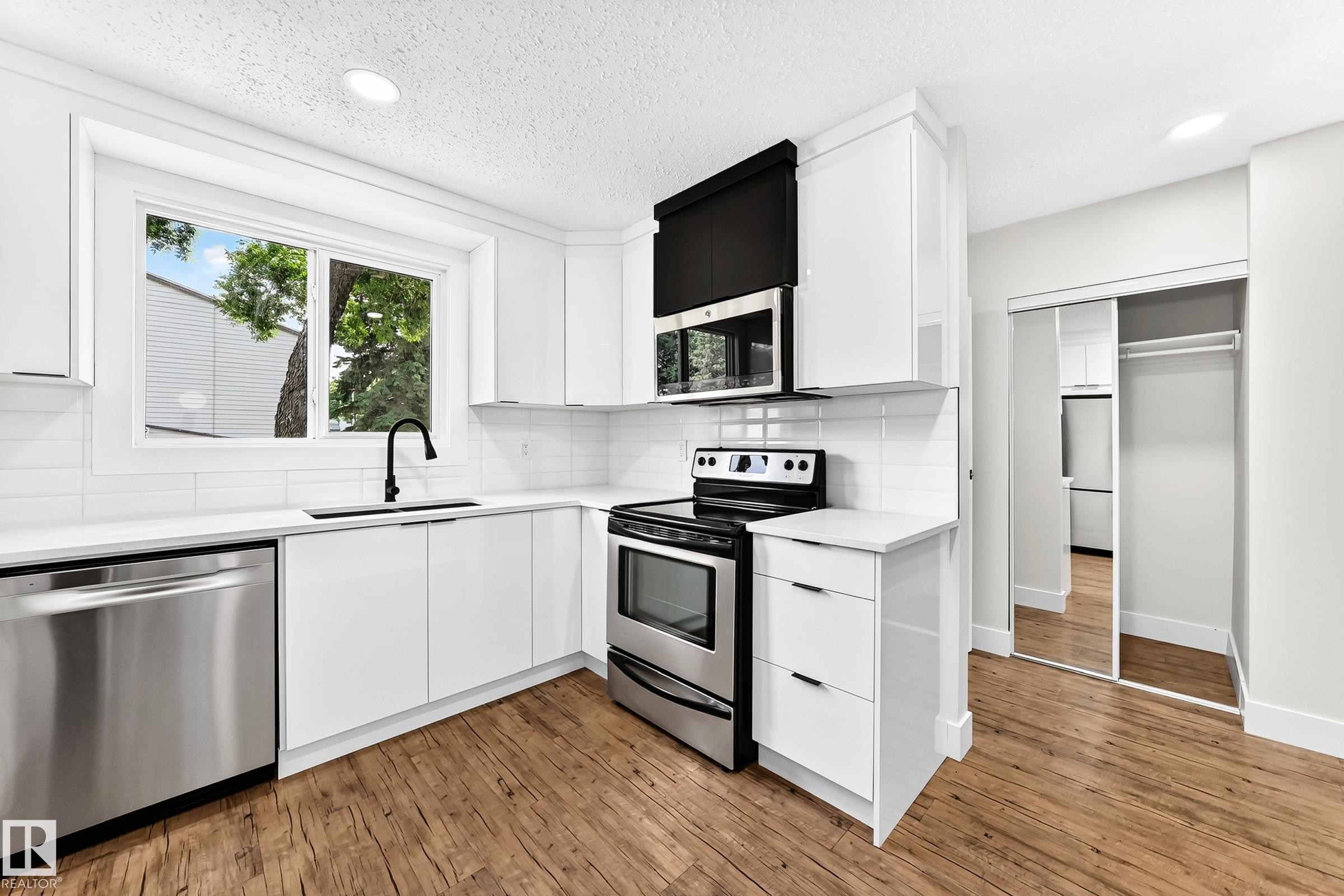 Modern kitchen featuring white cabinetry, stainless steel appliances, wood-finish flooring, and a subway tile backsplash - 3119 144 Avenue Nw, Edmonton, AB - Indoor Photo Showing Kitchen With Upgraded Kitchen