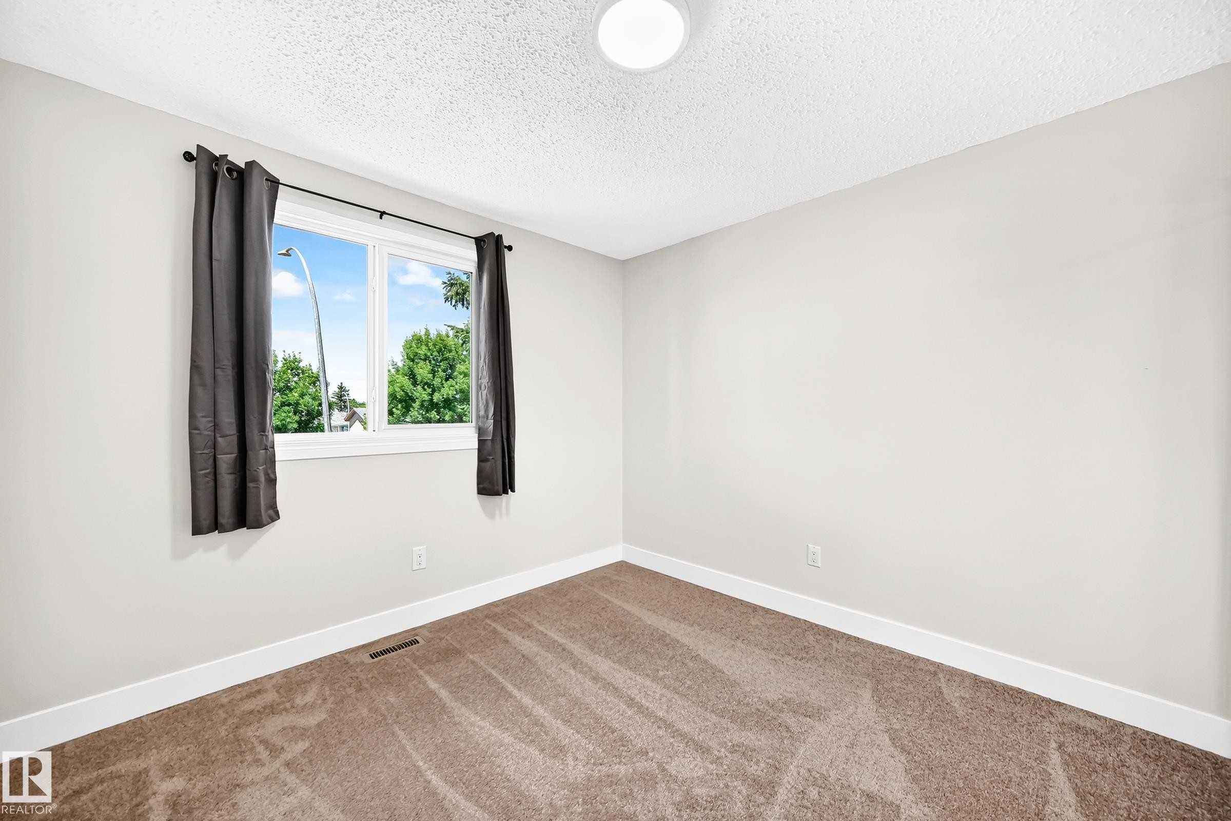 Bright room featuring a large window, neutral wall paint, white trim, and textured carpet flooring - 3119 144 Avenue Nw, Edmonton, AB - Indoor Photo Showing Other Room