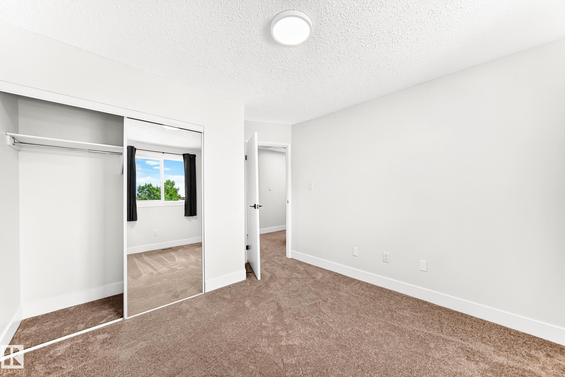 Carpeted room featuring a mirrored sliding closet door, white walls, and a round flush-mount ceiling light - 3119 144 Avenue Nw, Edmonton, AB - Indoor Photo Showing Other Room
