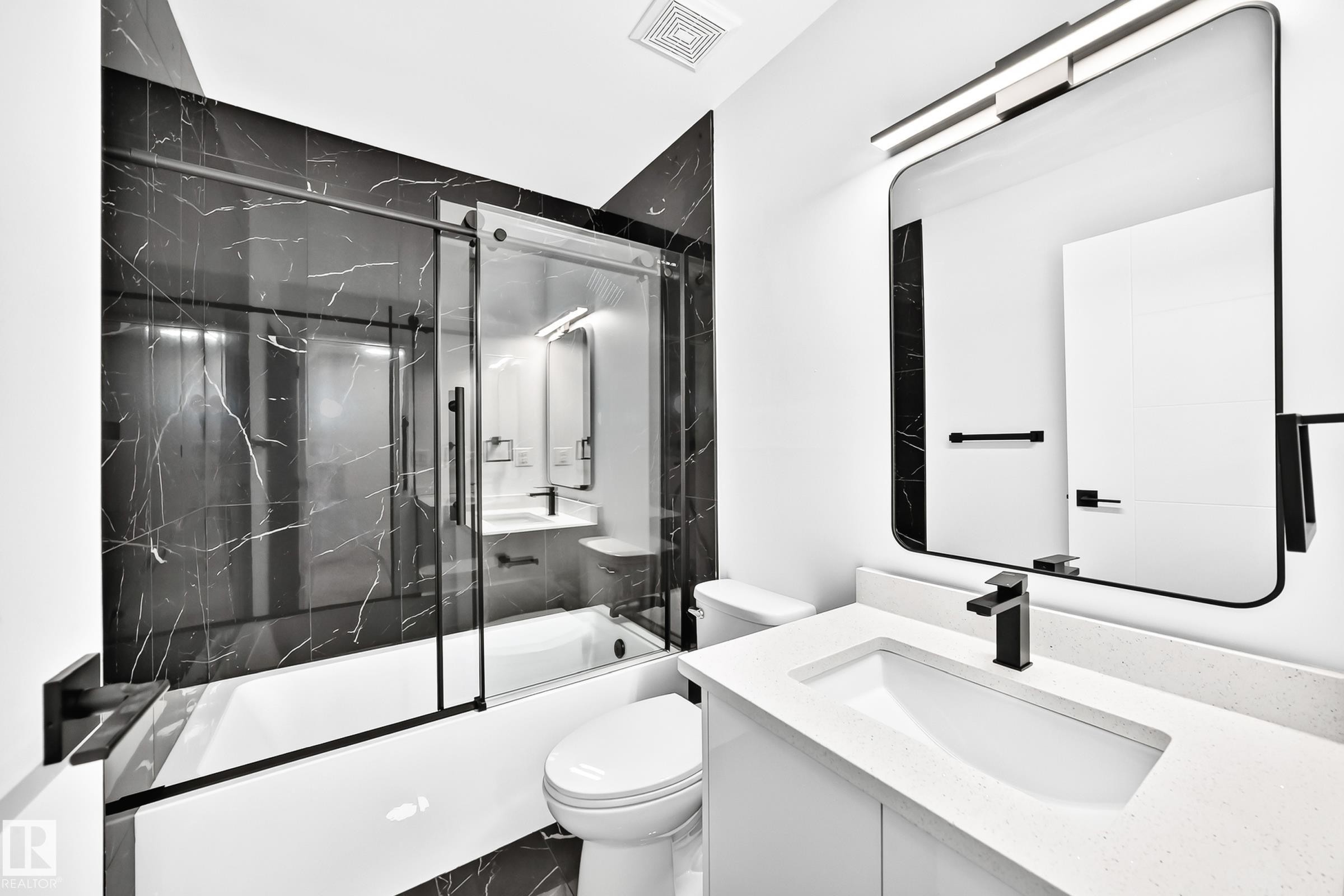 Contemporary bathroom featuring a dark marble-patterned shower surround with a sliding glass door, a white rectangular bathtub, a white vanity with a recessed sink, a rectangular mirror with rounded corners, and matte black fixtures - 3119 144 Avenue Nw, Edmonton, AB - Indoor Photo Showing Bathroom
