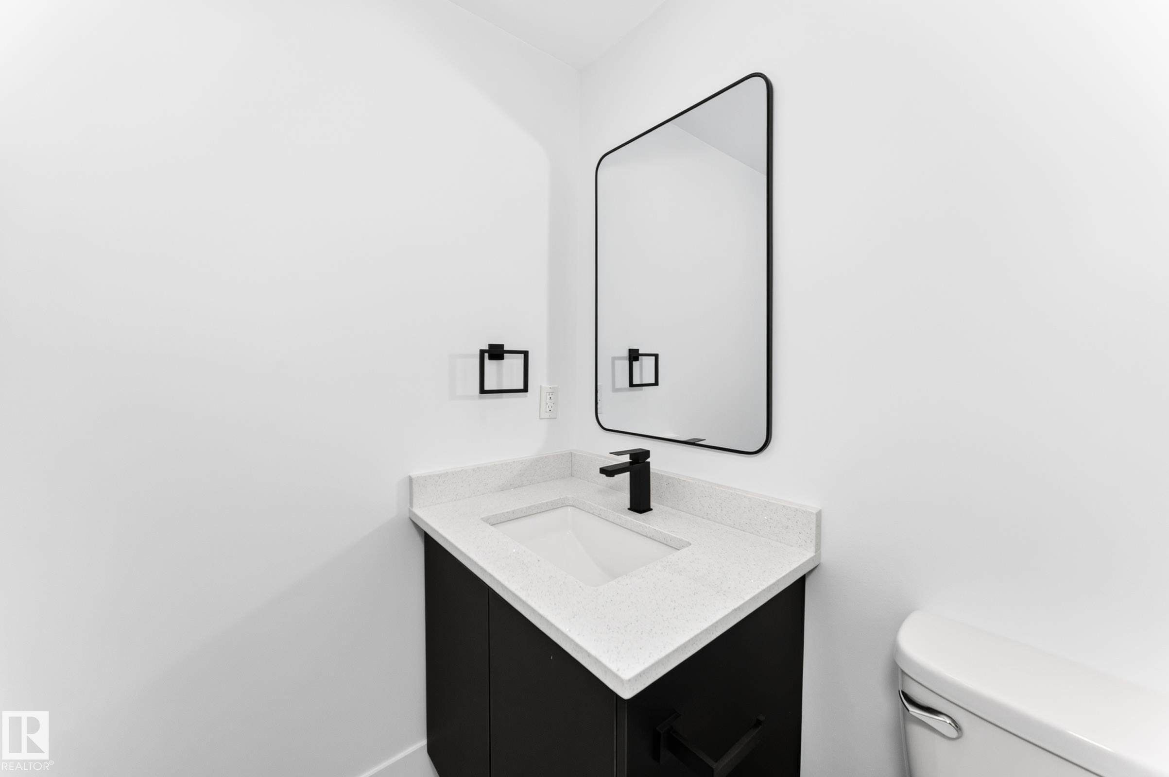 Modern vanity with a white countertop and integrated sink, matte black faucet, and coordinating black-framed mirror - 3119 144 Avenue Nw, Edmonton, AB - Indoor Photo Showing Bathroom