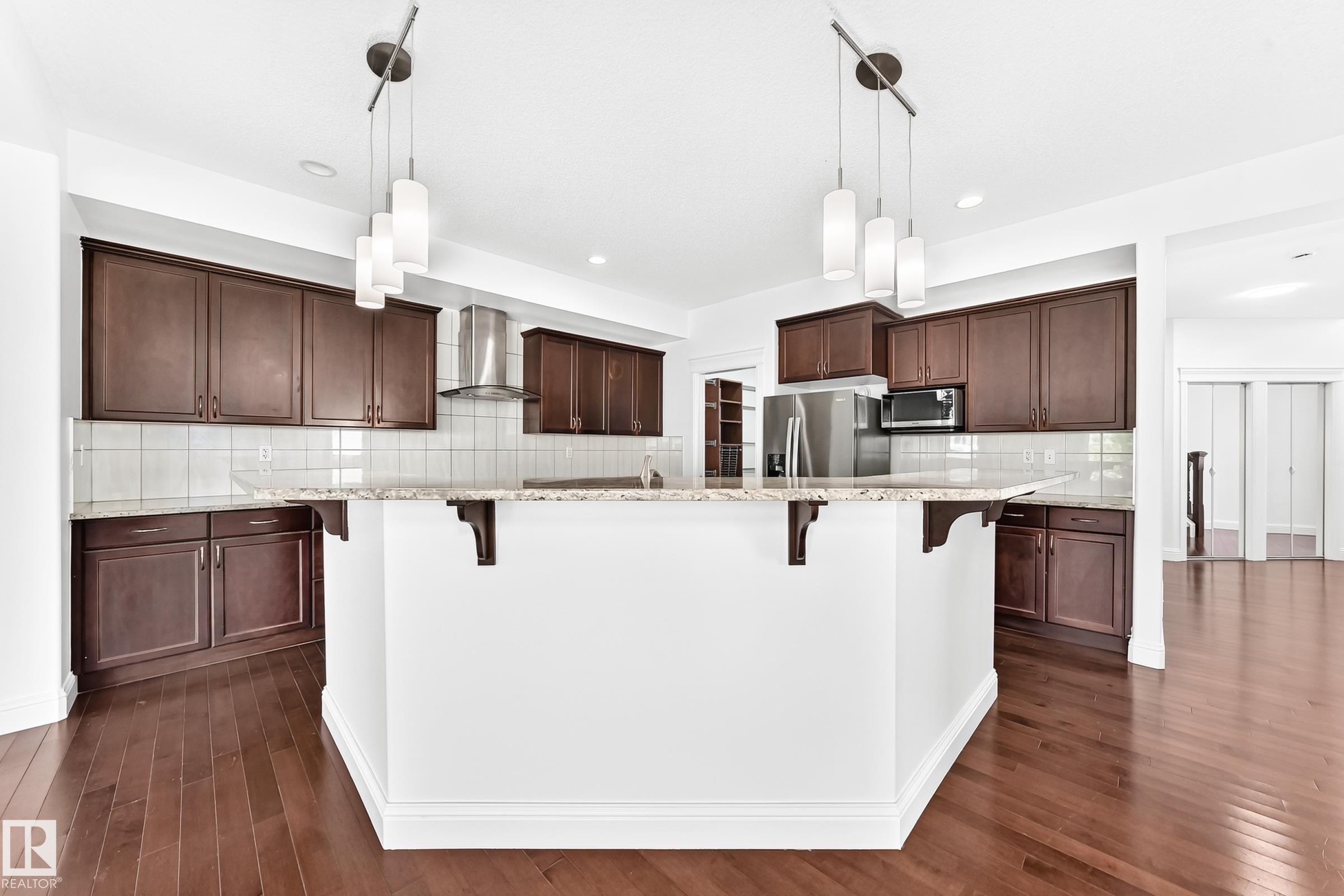 Kitchen island with white base and granite countertop, featuring dark wood-finish cabinetry, stainless steel appliances, and wood-finish flooring - 1663 Rutherford Road Sw, Edmonton, AB - Indoor Photo Showing Kitchen With Upgraded Kitchen