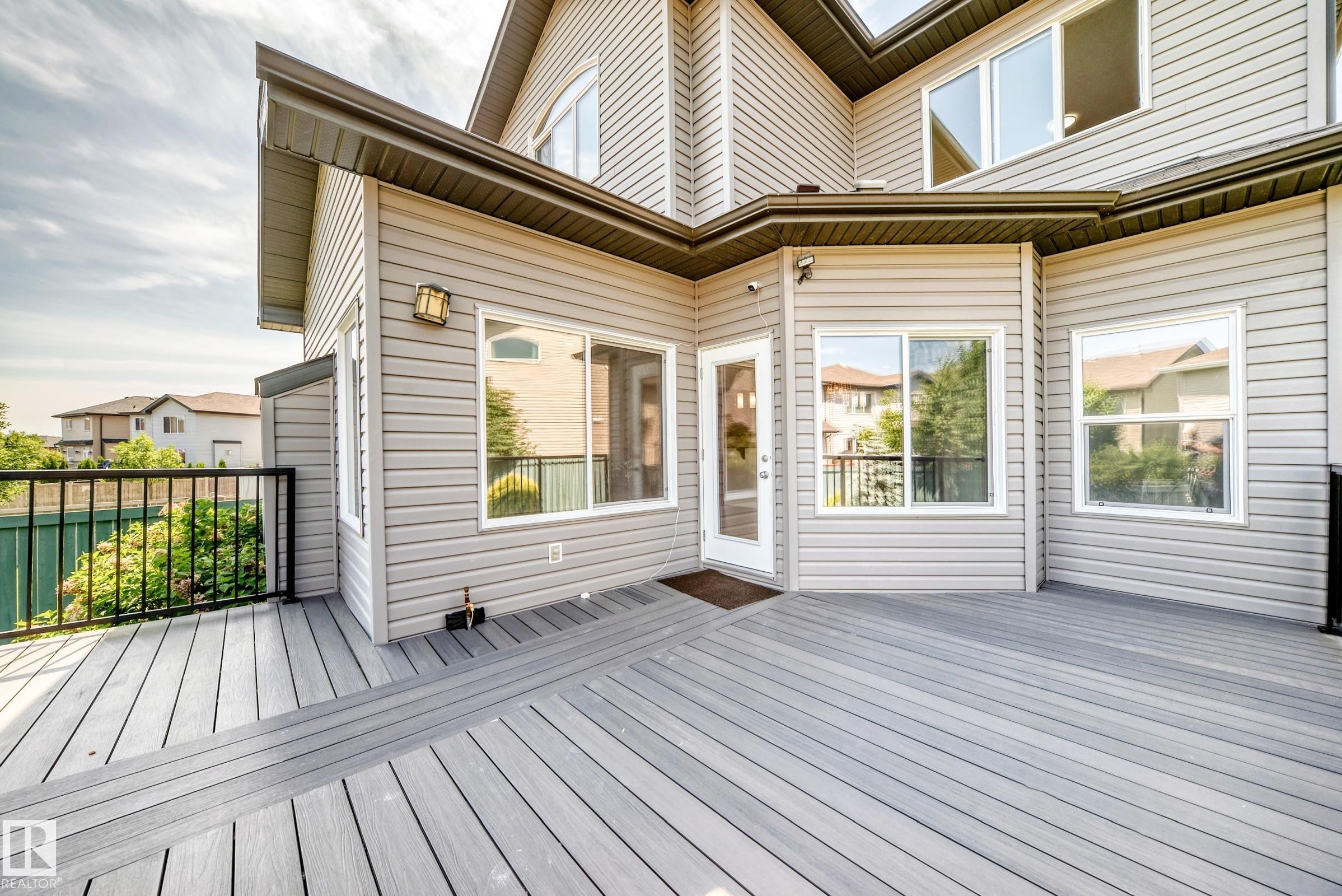 Spacious grey composite deck with black metal railing, featuring light-colored horizontal siding and multiple large windows - 1663 Rutherford Road Sw, Edmonton, AB - Outdoor With Deck Patio Veranda With Exterior
