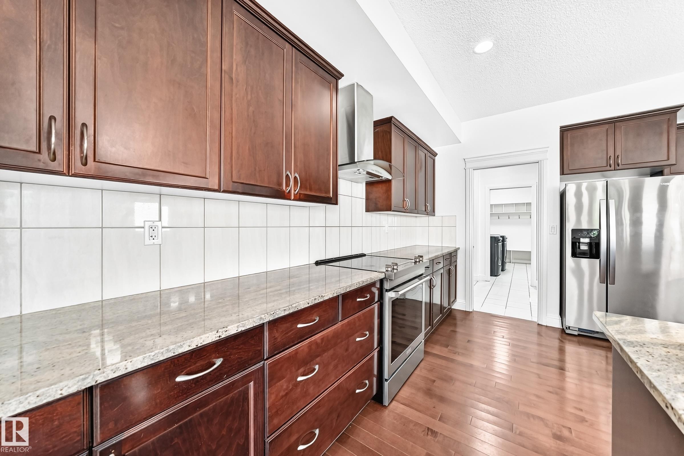 Kitchen featuring wood-finish flooring, dark wood cabinetry, light-toned countertops, and a white tile backsplash - 1663 Rutherford Road Sw, Edmonton, AB - Indoor Photo Showing Kitchen With Stainless Steel Kitchen With Upgraded Kitchen
