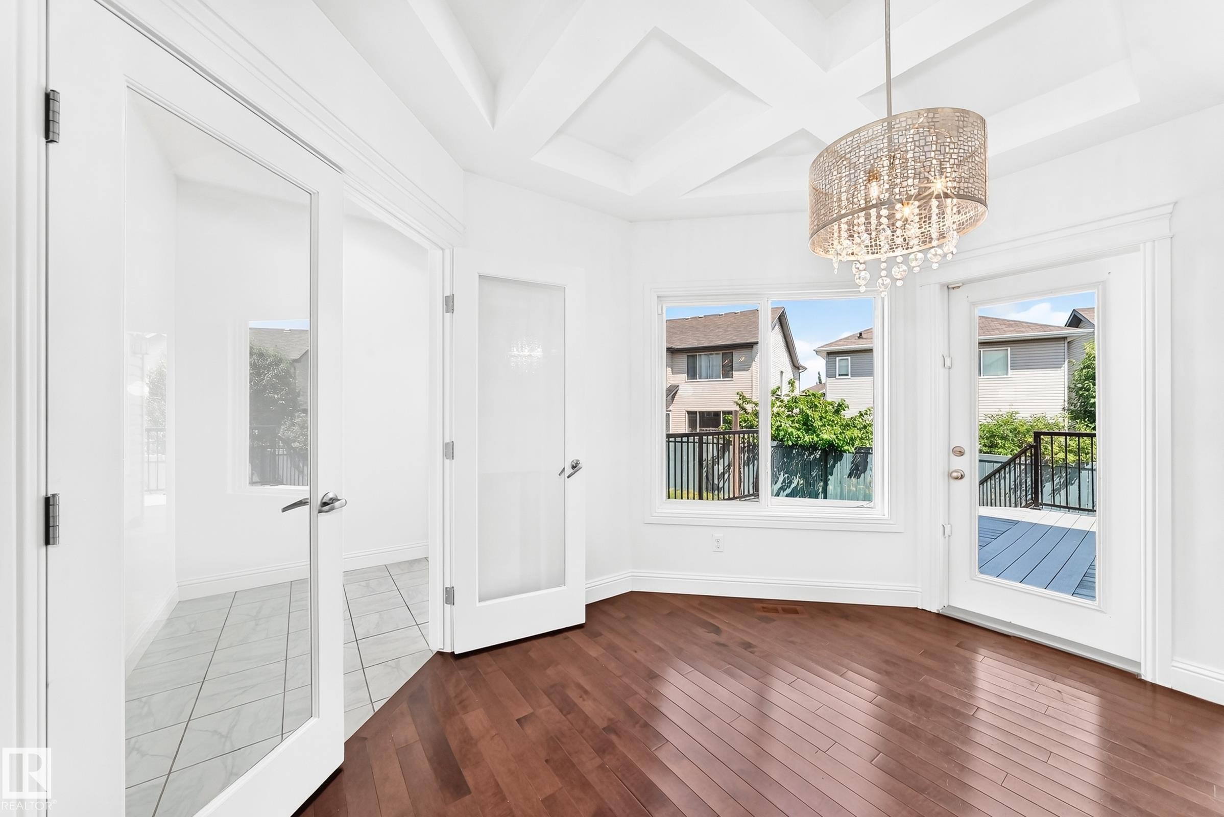 Rich wood-finish flooring complements a coffered ceiling with a decorative chandelier - 1663 Rutherford Road Sw, Edmonton, AB - Indoor Photo Showing Other Room