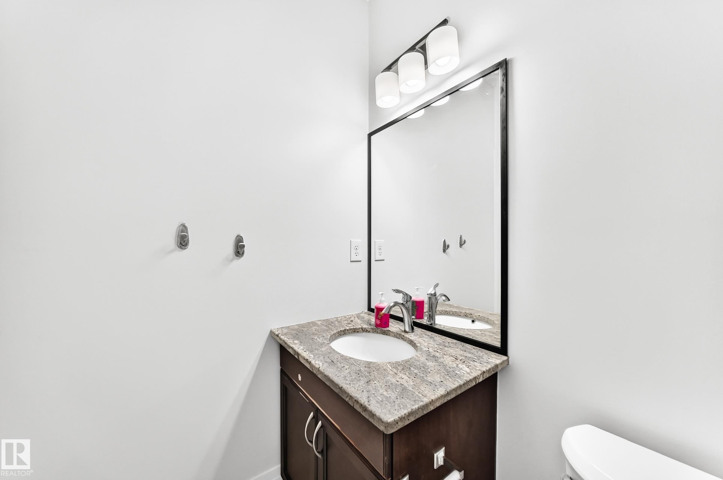 Bathroom vanity featuring a dark wood-finish cabinet with silver hardware, a light-toned stone countertop, and an undermount sink - 1663 Rutherford Road Sw, Edmonton, AB - Indoor Photo Showing Bathroom