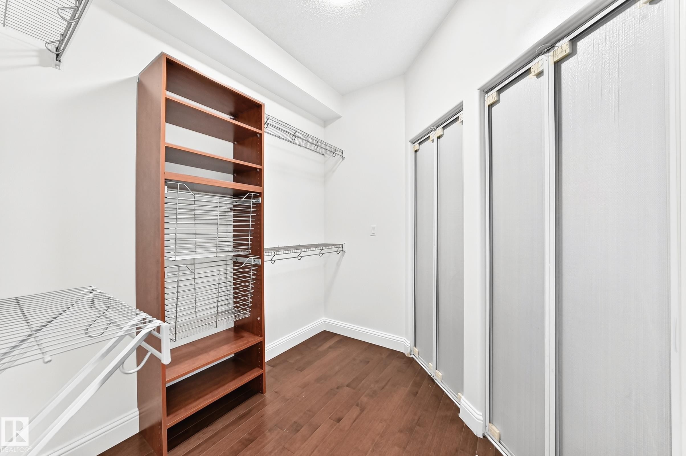 Walk-in closet featuring wood-finish flooring, built-in shelving, wire rack organizers, chrome hanging rods, and bi-fold closet doors - 1663 Rutherford Road Sw, Edmonton, AB - Indoor
