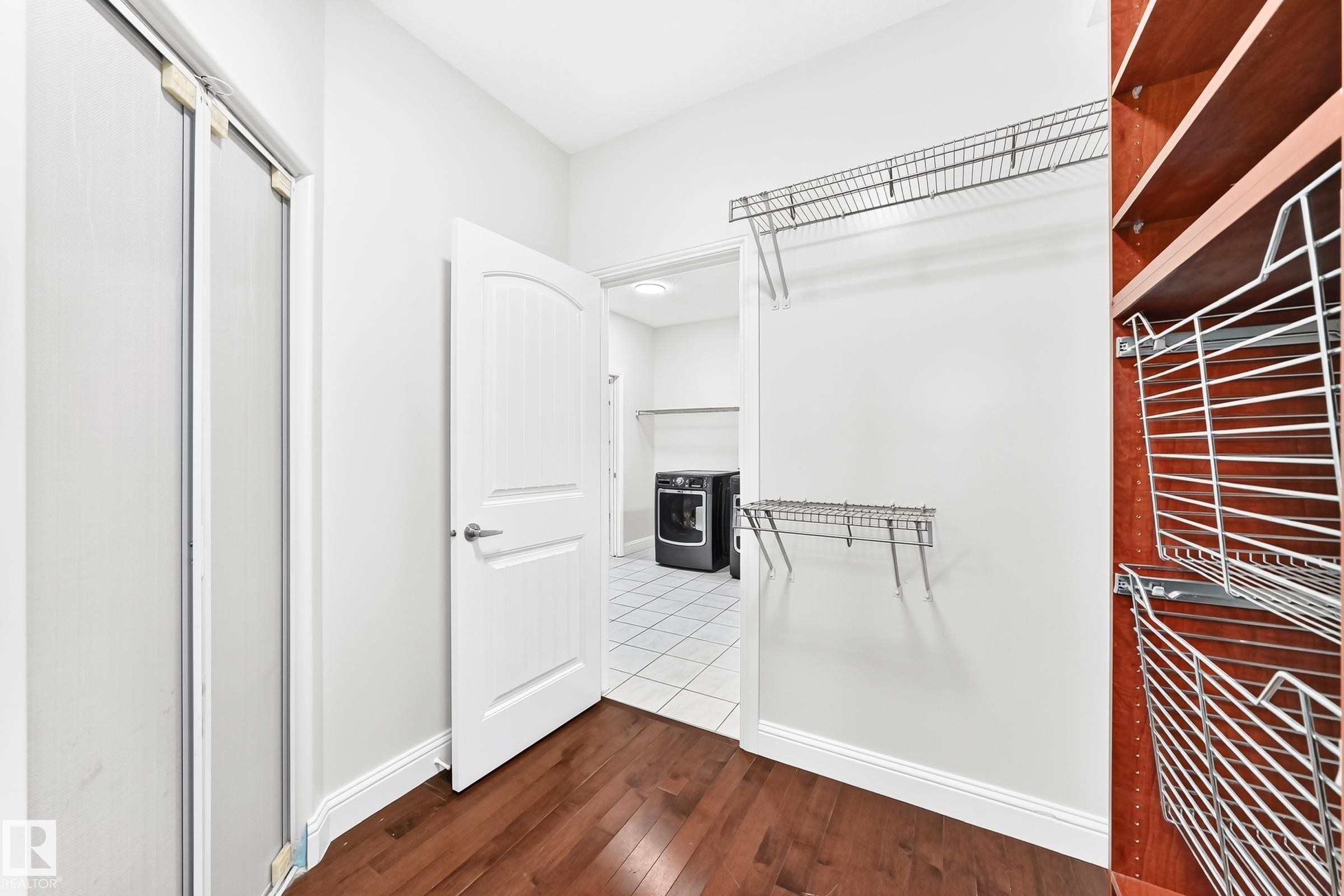 Expansive closet with rich wood-finish flooring, white walls, and a white arched panel door - 1663 Rutherford Road Sw, Edmonton, AB - Indoor