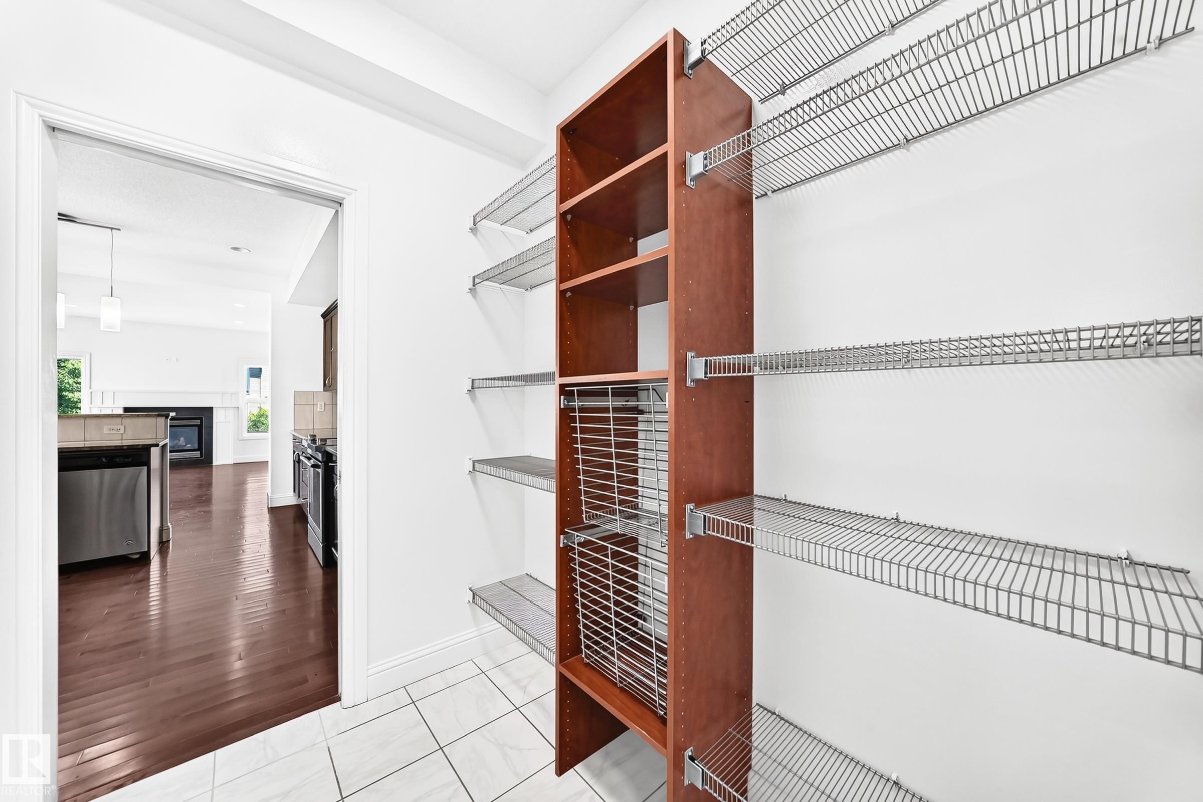 Pantry featuring white tile flooring, extensive wire shelving, a built-in wood-finish shelving unit, and integrated wire baskets - 1663 Rutherford Road Sw, Edmonton, AB - Indoor
