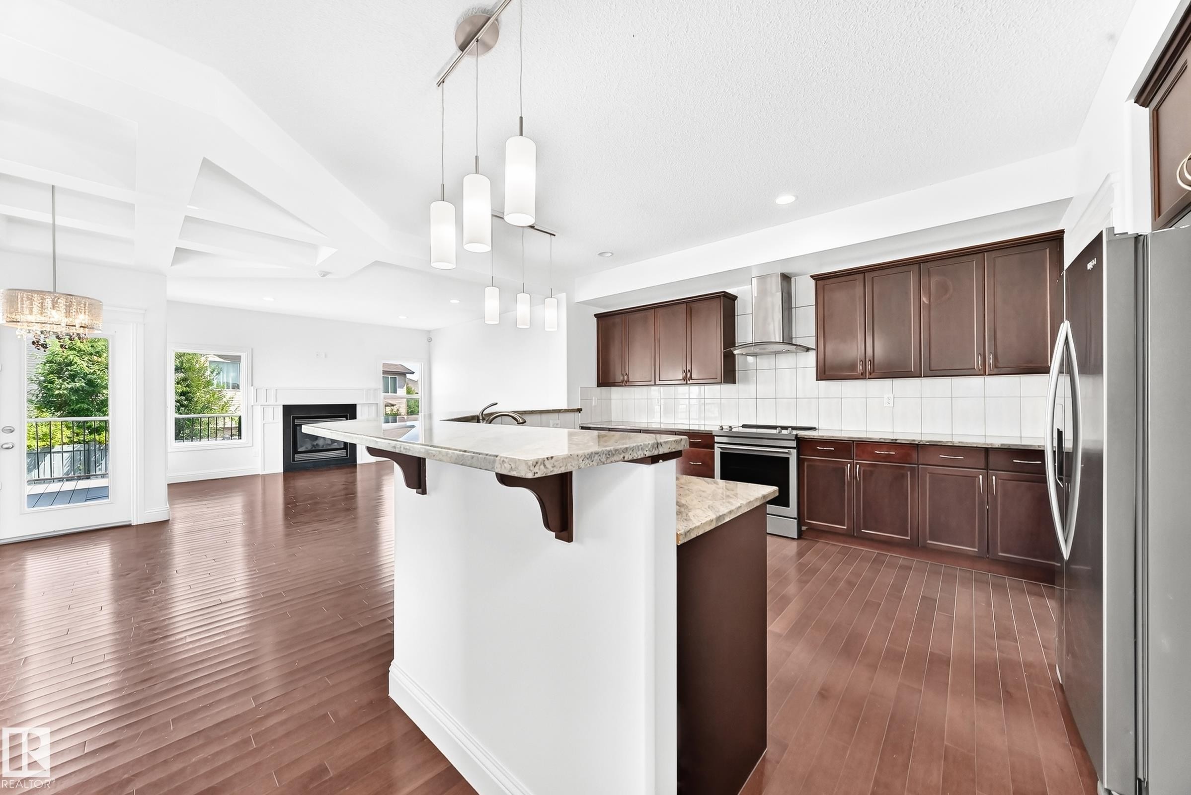 Open-concept kitchen featuring dark wood cabinetry, stainless steel appliances, and a central island with a granite-style countertop - 1663 Rutherford Road Sw, Edmonton, AB - Indoor Photo Showing Kitchen With Upgraded Kitchen