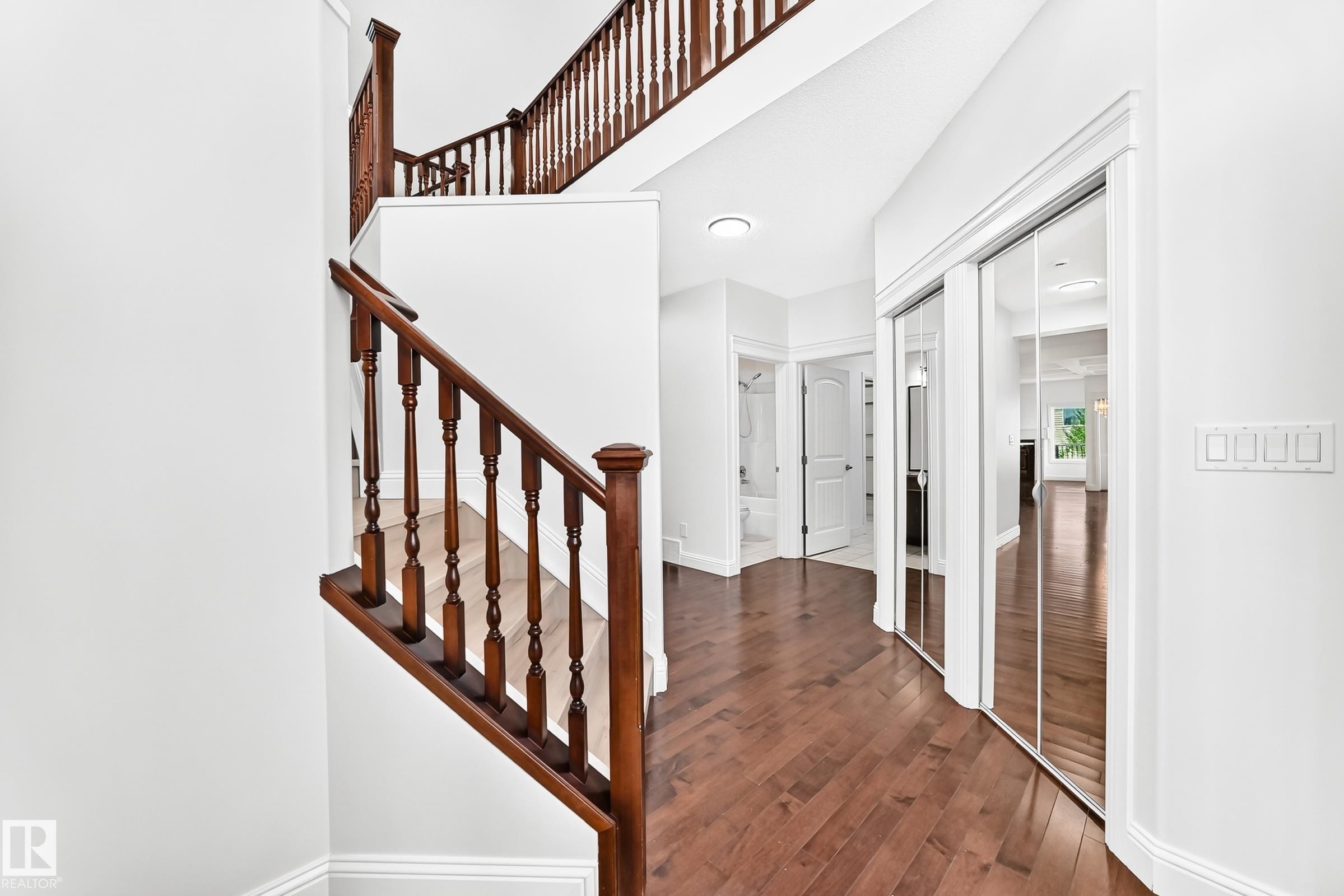 Two-story staircase with dark wood balusters and handrails, complemented by wood-finish flooring, white walls, and mirrored closet doors - 1663 Rutherford Road Sw, Edmonton, AB - Indoor Photo Showing Other Room