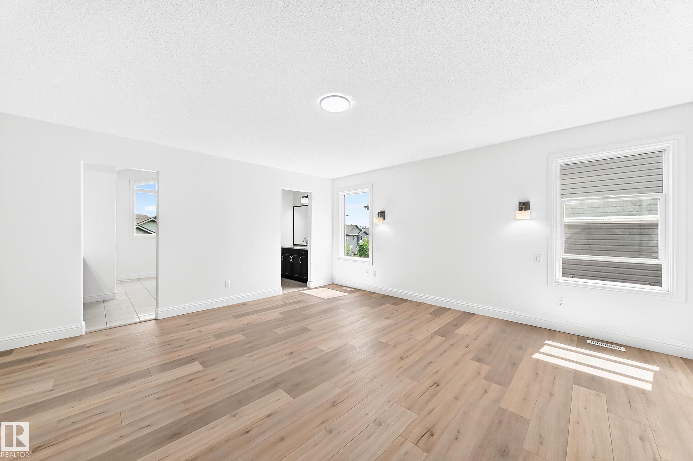 Spacious interior featuring wood-finish flooring, white walls, multiple windows, recessed lighting, and wall sconces - 1663 Rutherford Road Sw, Edmonton, AB - Indoor