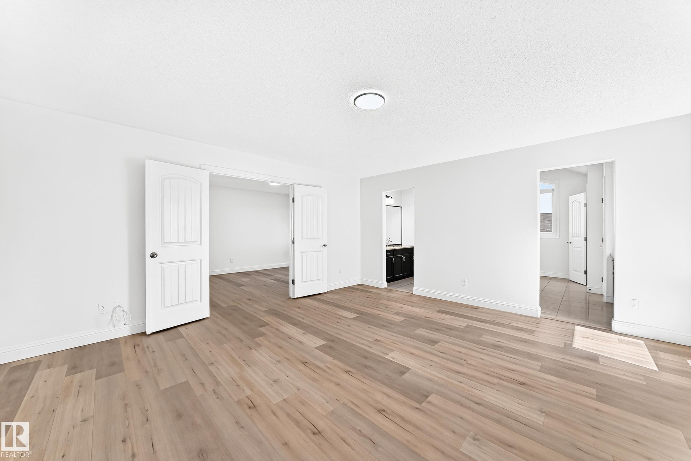 Spacious room featuring wood-finish flooring, white walls, and a contemporary ceiling light fixture - 1663 Rutherford Road Sw, Edmonton, AB - Indoor Photo Showing Other Room