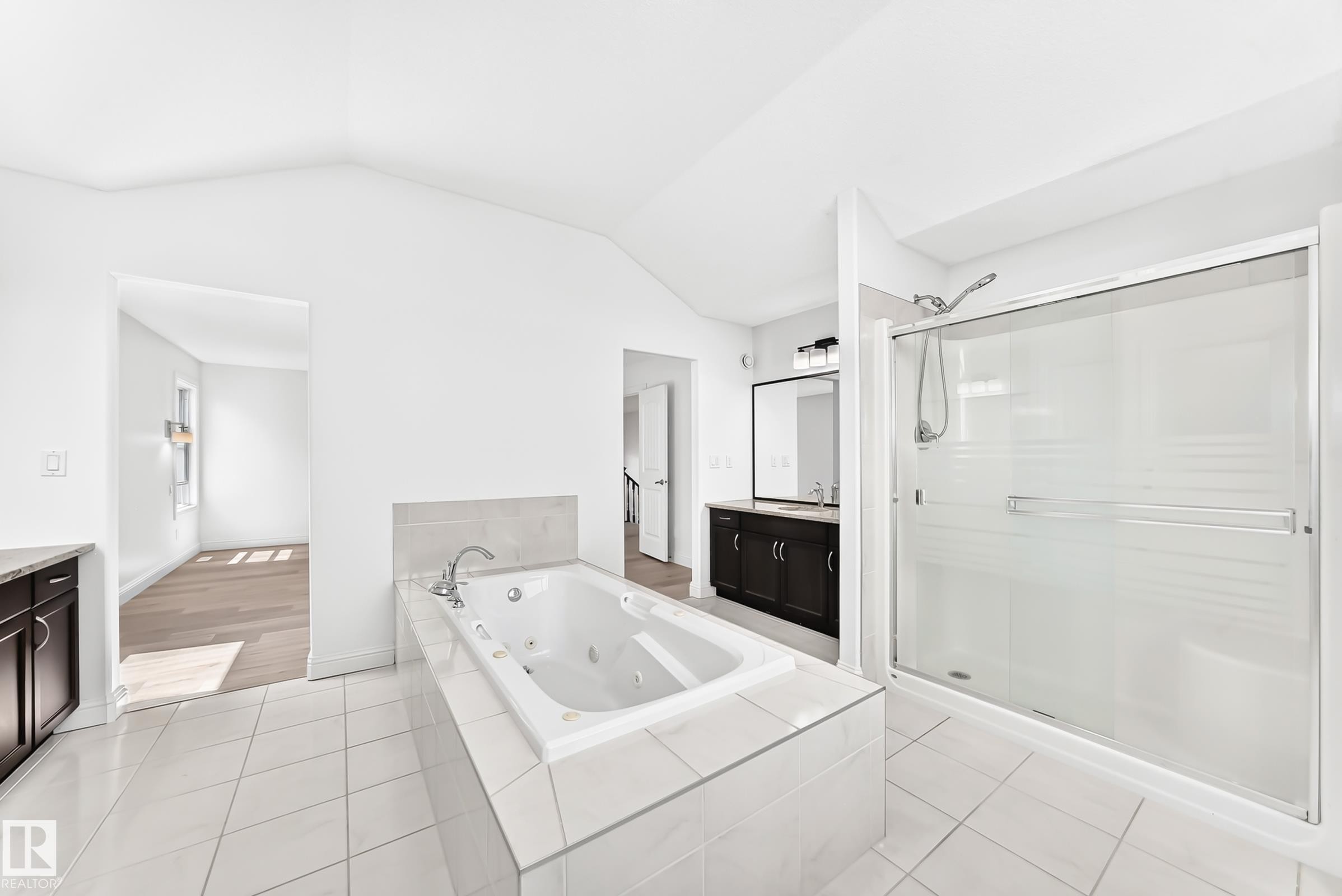 Bathroom featuring a jetted soaking tub with tiled surround, a glass-enclosed shower with sliding door, and a dual vanity with dark wood-finish cabinetry and a framed mirror - 1663 Rutherford Road Sw, Edmonton, AB - Indoor Photo Showing Bathroom