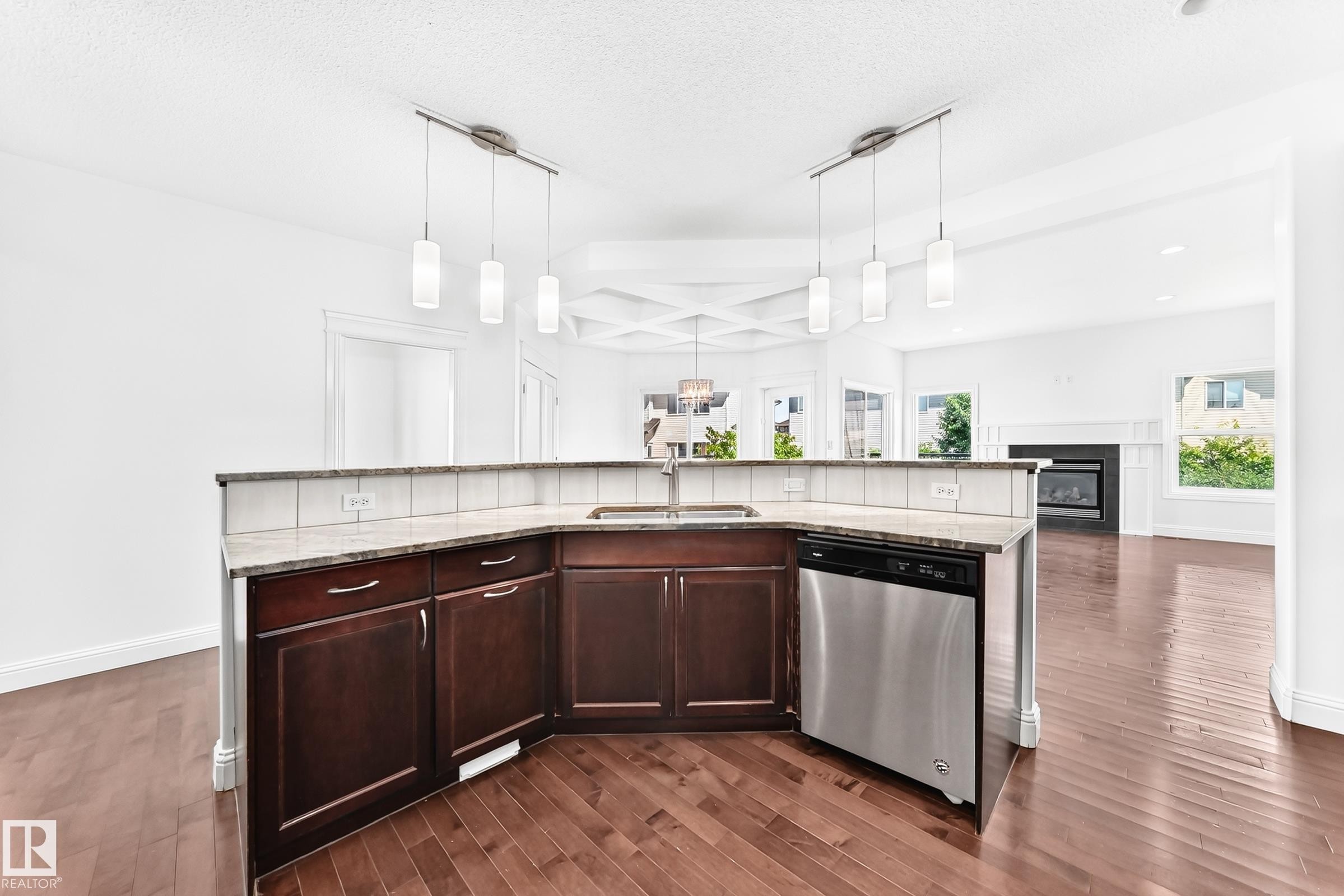 Kitchen island with dark wood cabinetry, a stainless steel dishwasher, and a double basin sink - 1663 Rutherford Road Sw, Edmonton, AB - Indoor Photo Showing Kitchen