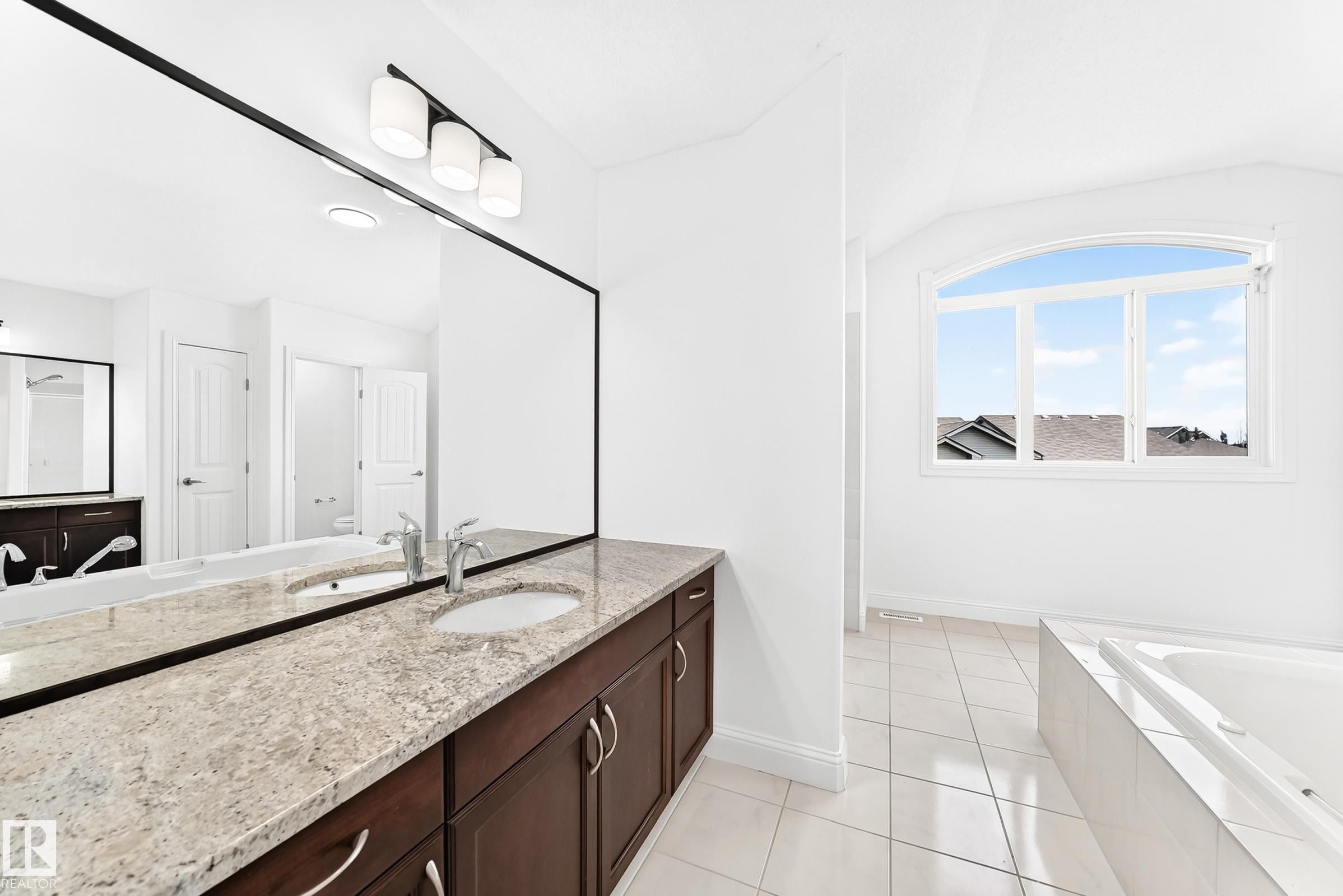 Double vanity featuring dark wood-finish cabinetry, light-toned stone countertops, and undermount sinks - 1663 Rutherford Road Sw, Edmonton, AB - Indoor Photo Showing Bathroom