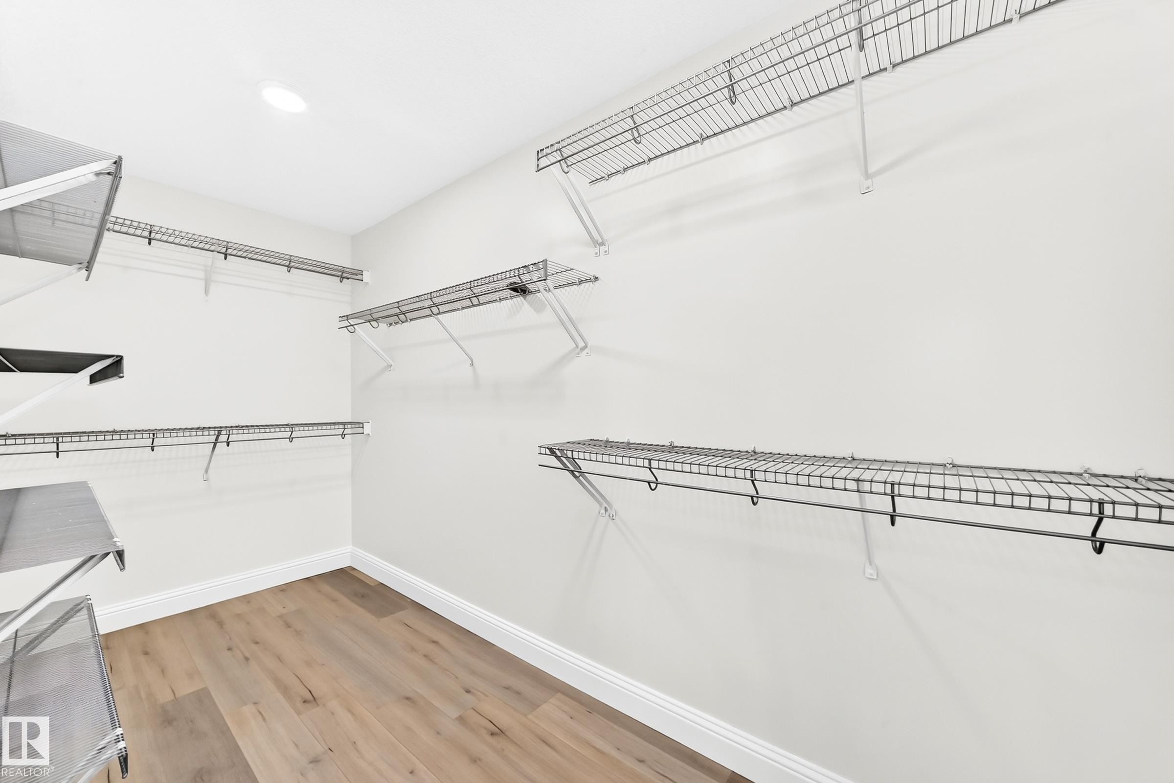 Spacious closet featuring multiple levels of wire shelving, integrated hanging rods, recessed ceiling lighting, light wood-finish flooring, and white baseboards - 1663 Rutherford Road Sw, Edmonton, AB - Indoor With Storage