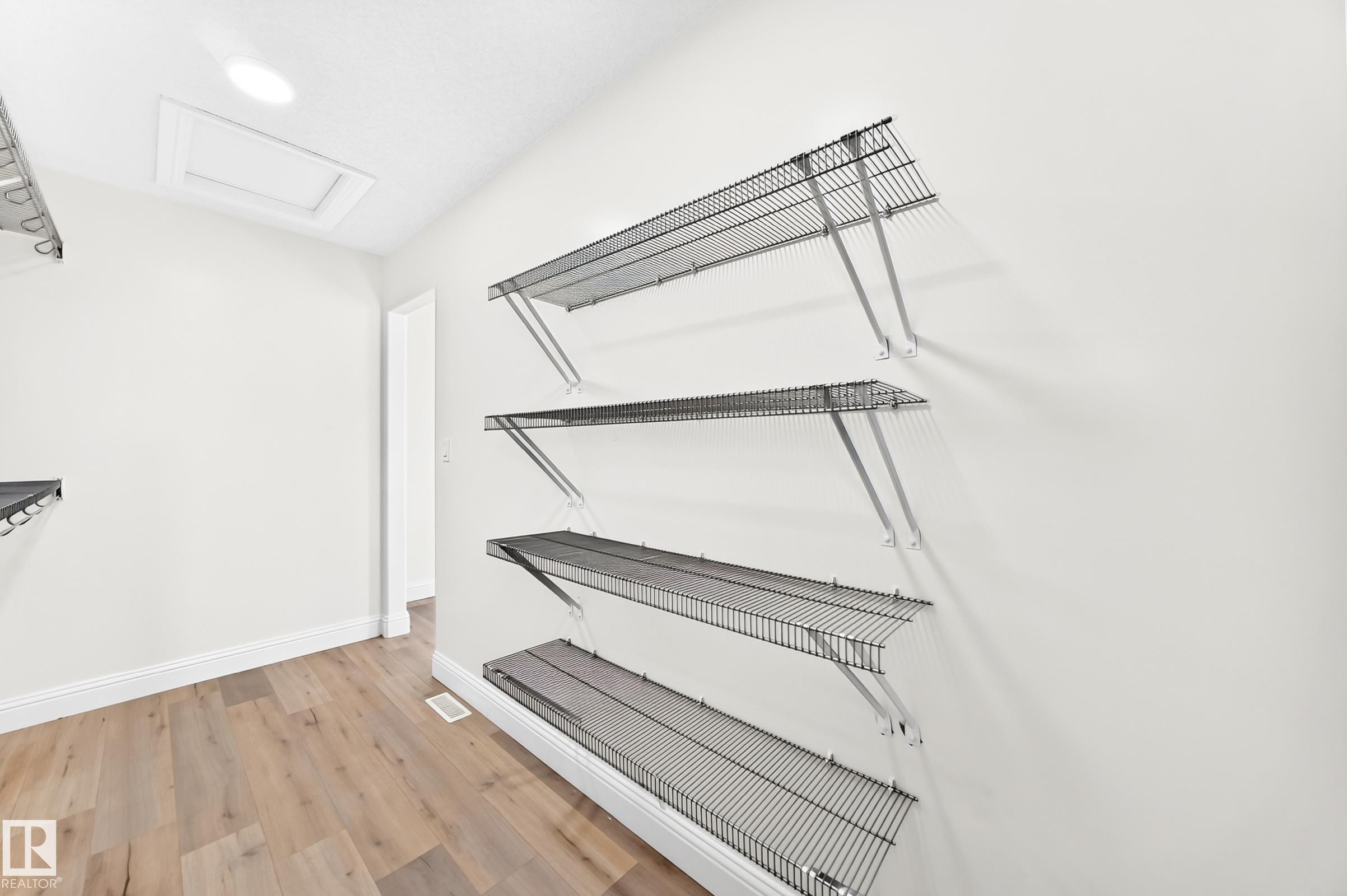 Utility room featuring wood-finish flooring, white walls, recessed ceiling lighting, and wire shelving - 1663 Rutherford Road Sw, Edmonton, AB - Indoor With Storage