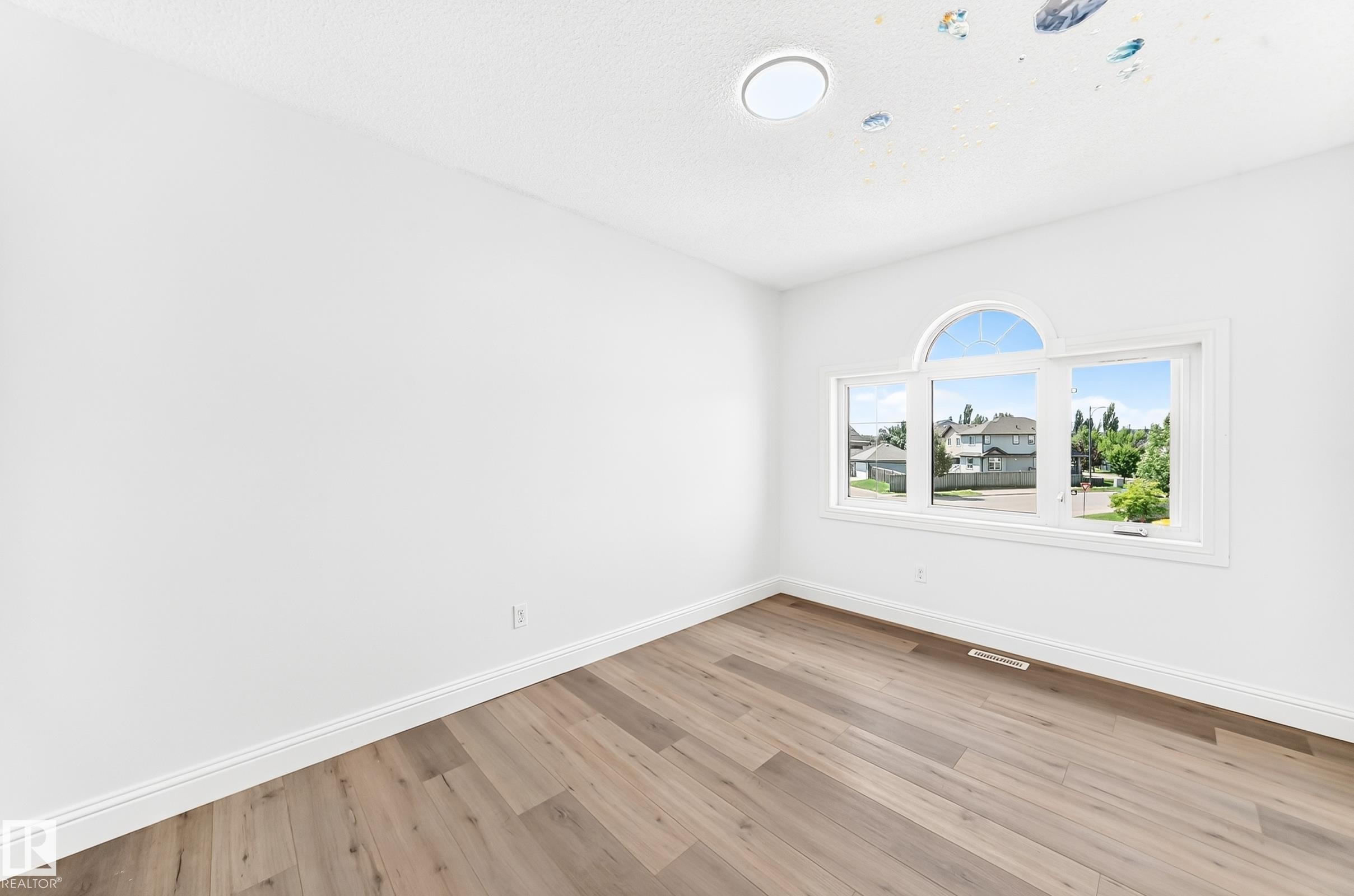 Room featuring a large arched window, wood-finish flooring, white baseboards, and a circular ceiling light fixture - 1663 Rutherford Road Sw, Edmonton, AB - Indoor Photo Showing Other Room