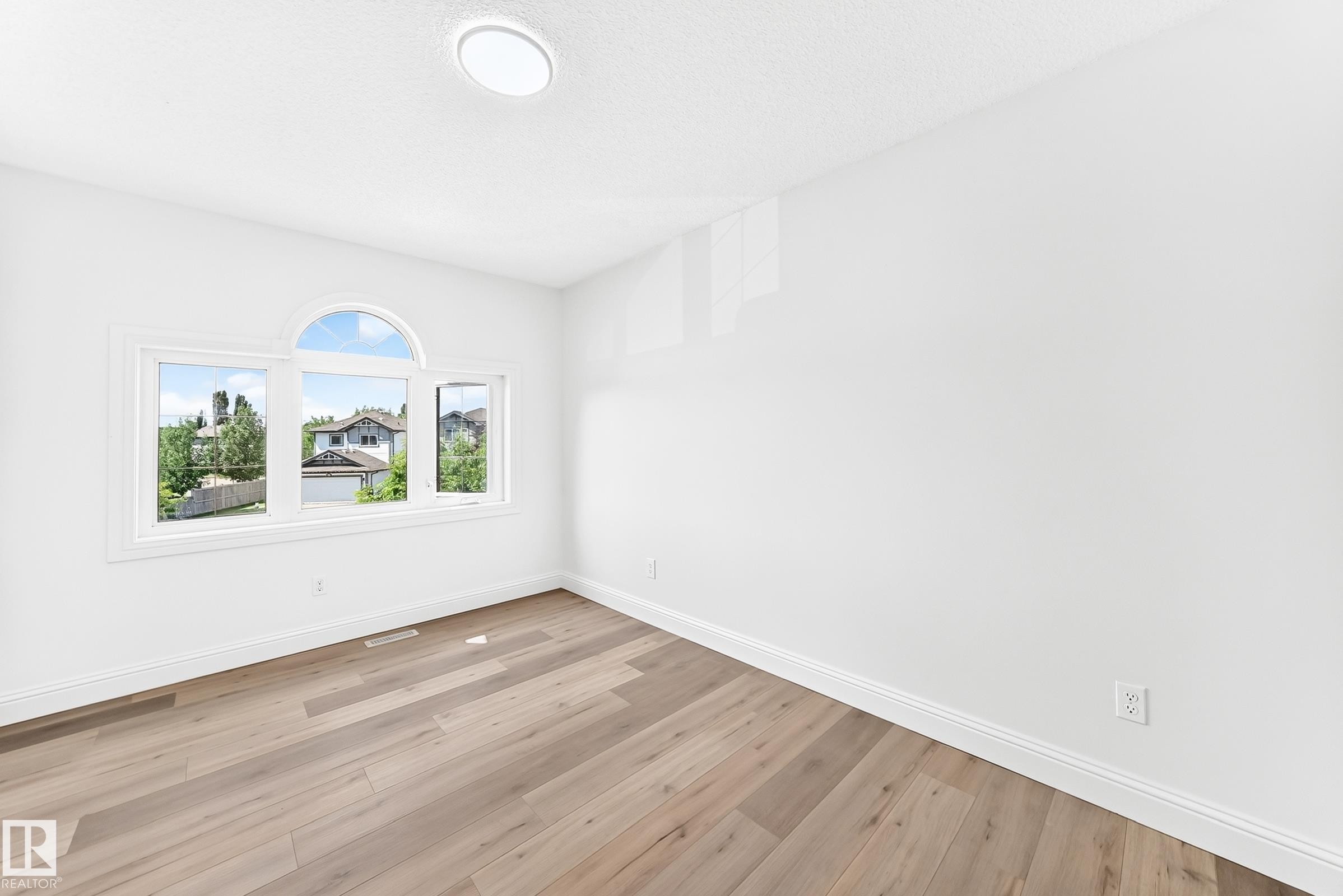 Bright room featuring light wood-finish flooring, white baseboards, and a prominent multi-pane window with an arched transom - 1663 Rutherford Road Sw, Edmonton, AB - Indoor Photo Showing Other Room