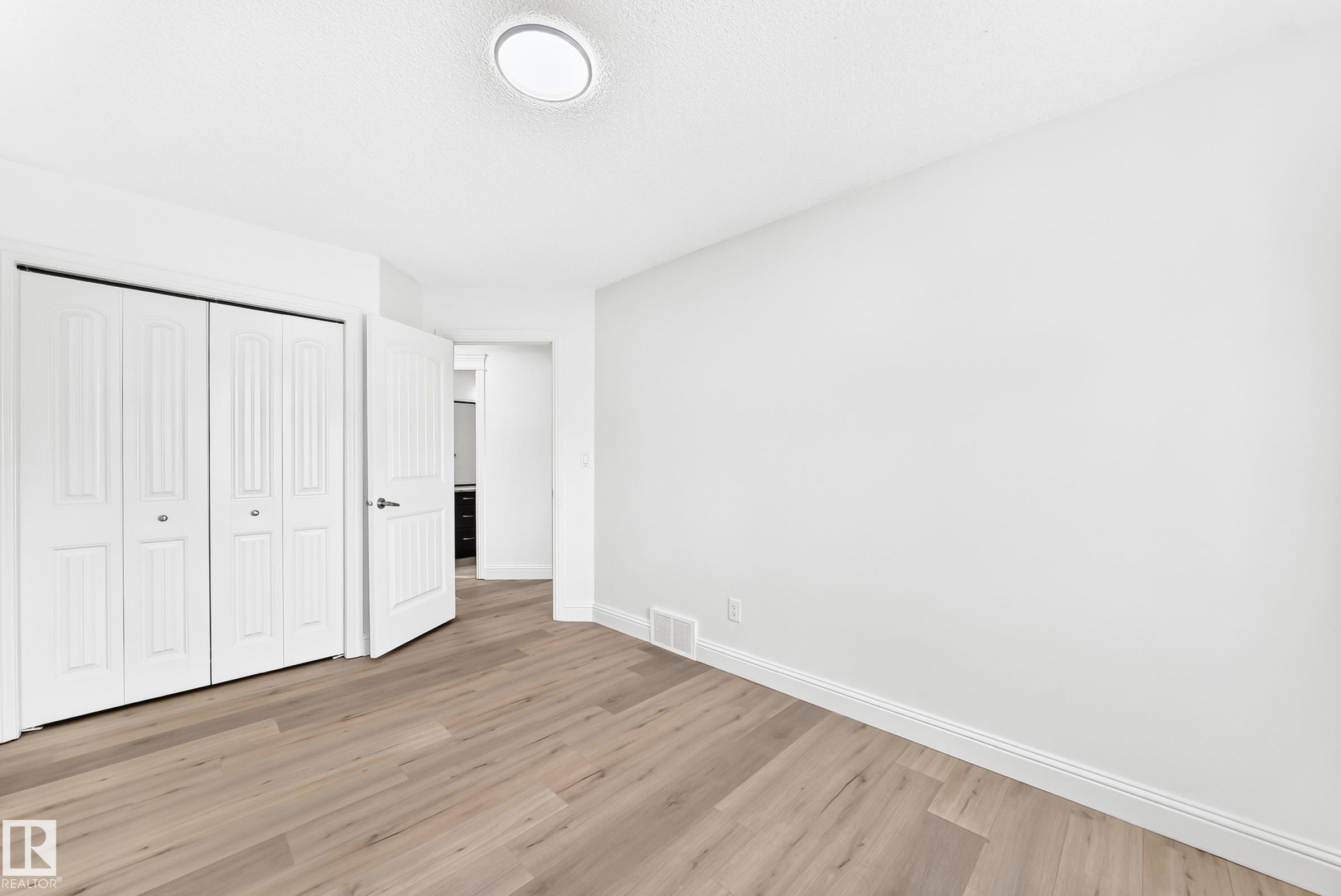 Room featuring wood-finish flooring, white baseboards, and a white ceiling with a flush-mount light fixture - 1663 Rutherford Road Sw, Edmonton, AB - Indoor Photo Showing Other Room
