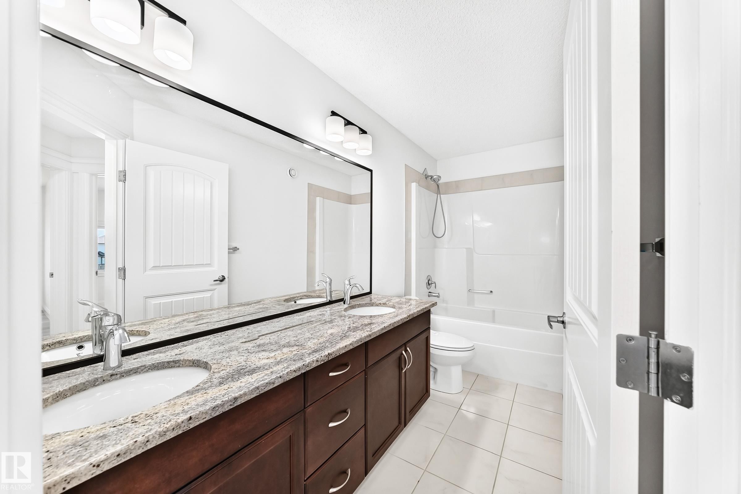 Bathroom featuring a double vanity with stone countertop, undermount sinks, chrome fixtures, and dark wood cabinetry - 1663 Rutherford Road Sw, Edmonton, AB - Indoor Photo Showing Bathroom