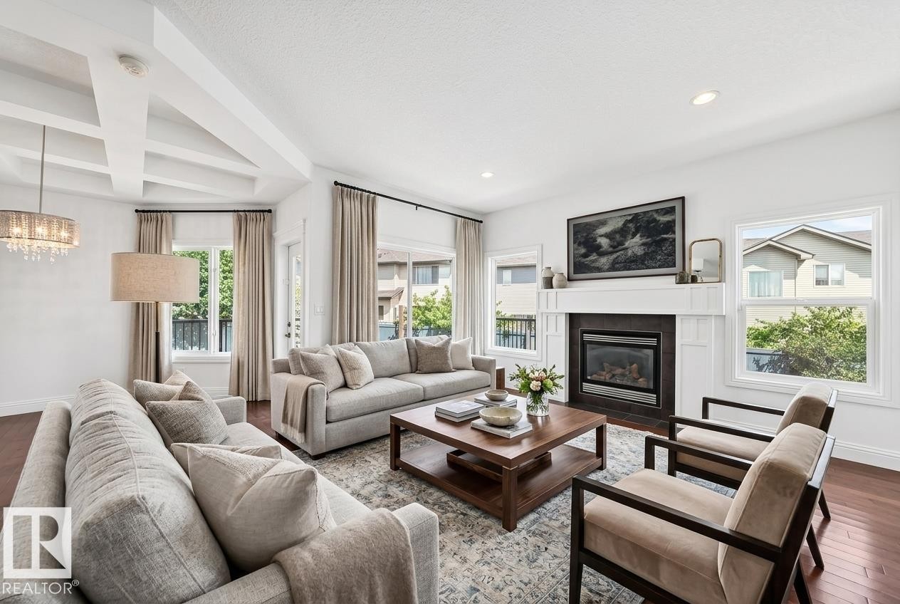 Spacious living room featuring rich wood-finish flooring, a coffered ceiling, and a prominent fireplace with a white mantel and dark tile surround - 1663 Rutherford Road Sw, Edmonton, AB - Indoor Photo Showing Living Room With Fireplace