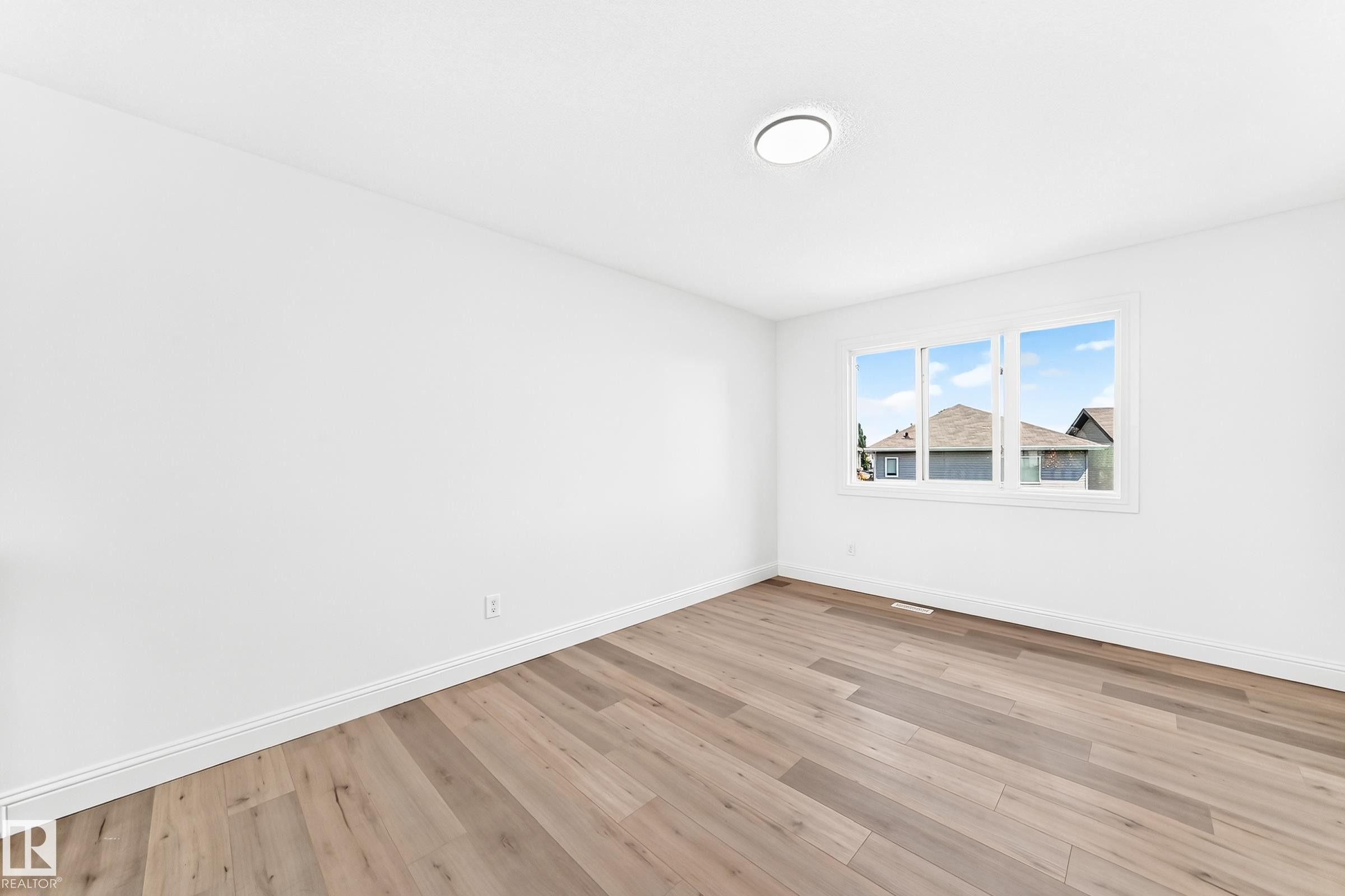 Spacious room featuring wood-finish flooring, white baseboards, and a three-pane window - 1663 Rutherford Road Sw, Edmonton, AB - Indoor Photo Showing Other Room