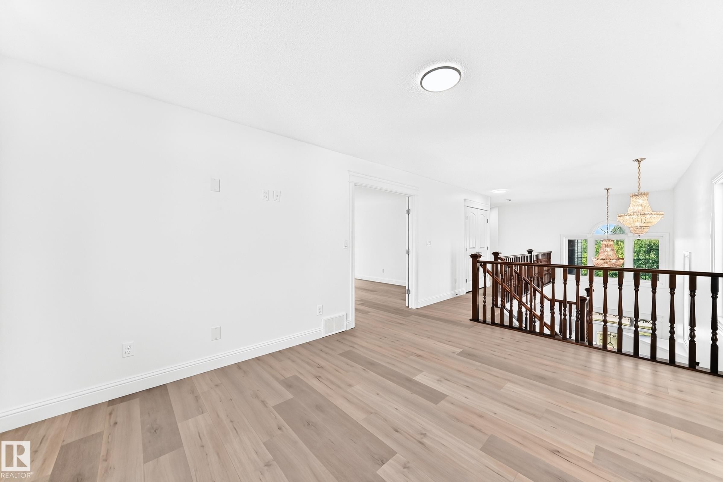 Spacious upper-level landing featuring light wood-finish flooring, white walls, and a dark wood staircase railing - 1663 Rutherford Road Sw, Edmonton, AB - Indoor Photo Showing Other Room