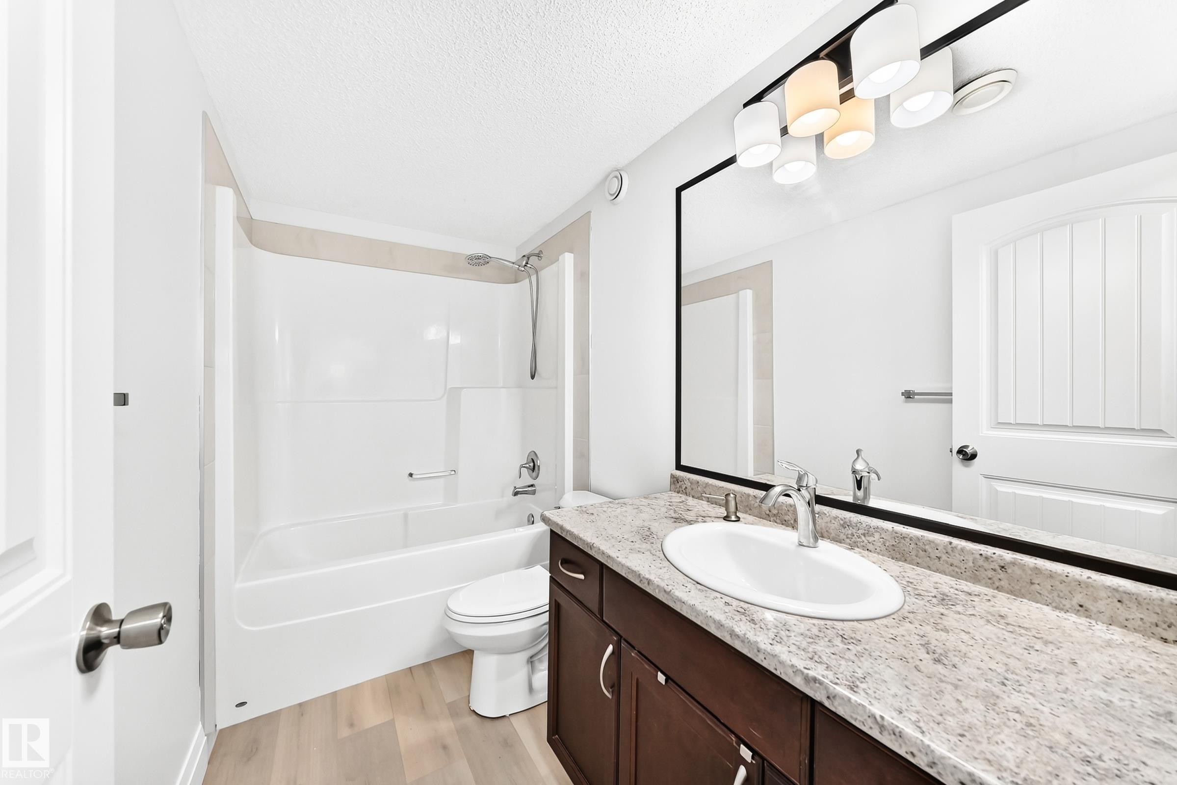 Bathroom featuring a vanity with a light-toned speckled countertop, an undermount sink with chrome fixtures, a large framed mirror, and a multi-bulb vanity light - 1663 Rutherford Road Sw, Edmonton, AB - Indoor Photo Showing Bathroom