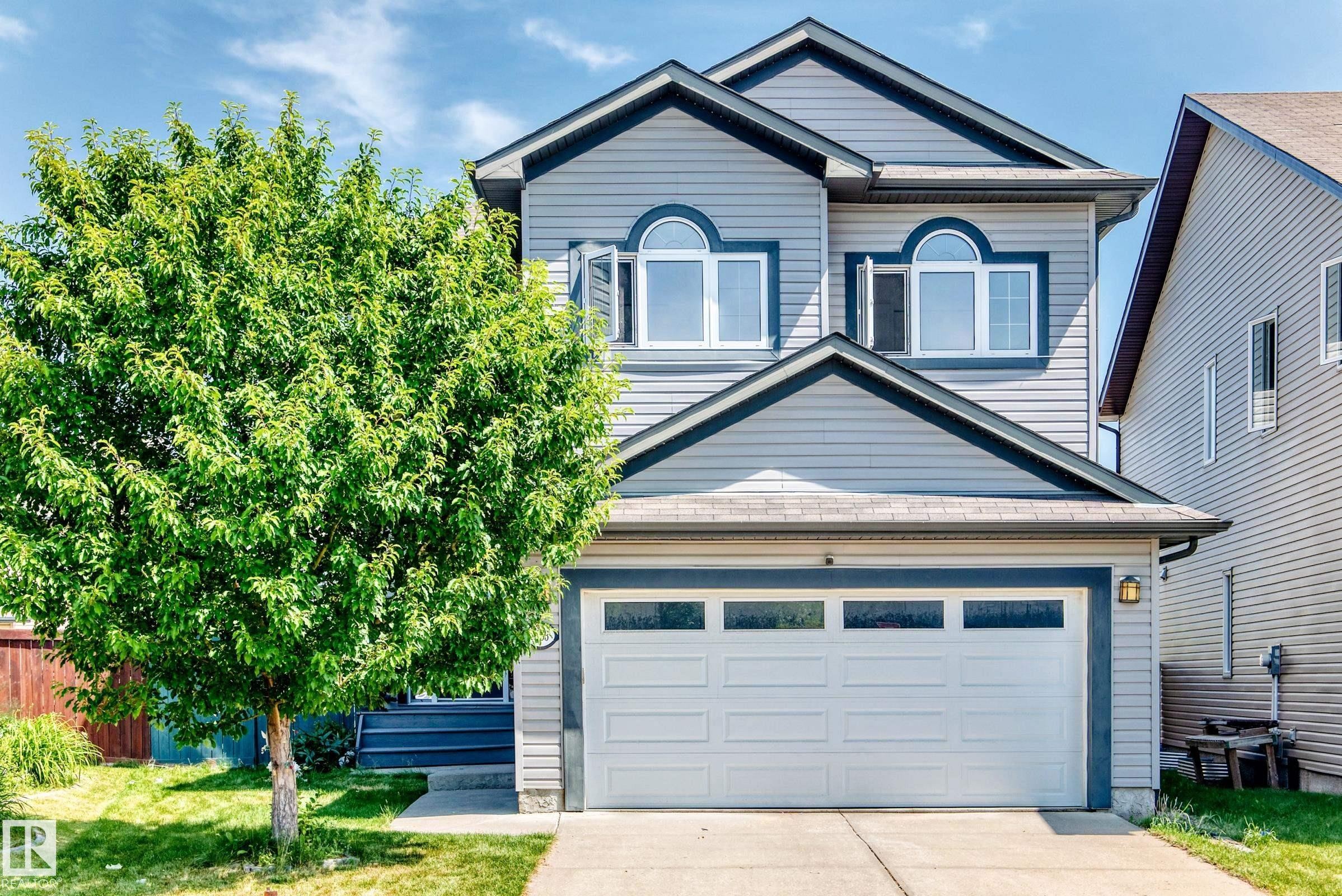 Two-story home featuring light grey siding with dark grey trim accents, a two-car garage with frosted pane windows, and arched windows on the upper level - 1663 Rutherford Road Sw, Edmonton, AB - Outdoor