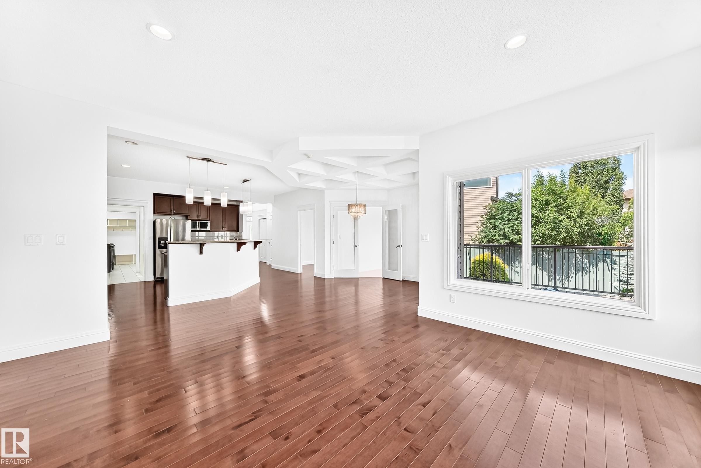 Spacious open-concept living area featuring rich wood-finish flooring, recessed lighting, and a coffered ceiling detail - 1663 Rutherford Road Sw, Edmonton, AB - Indoor