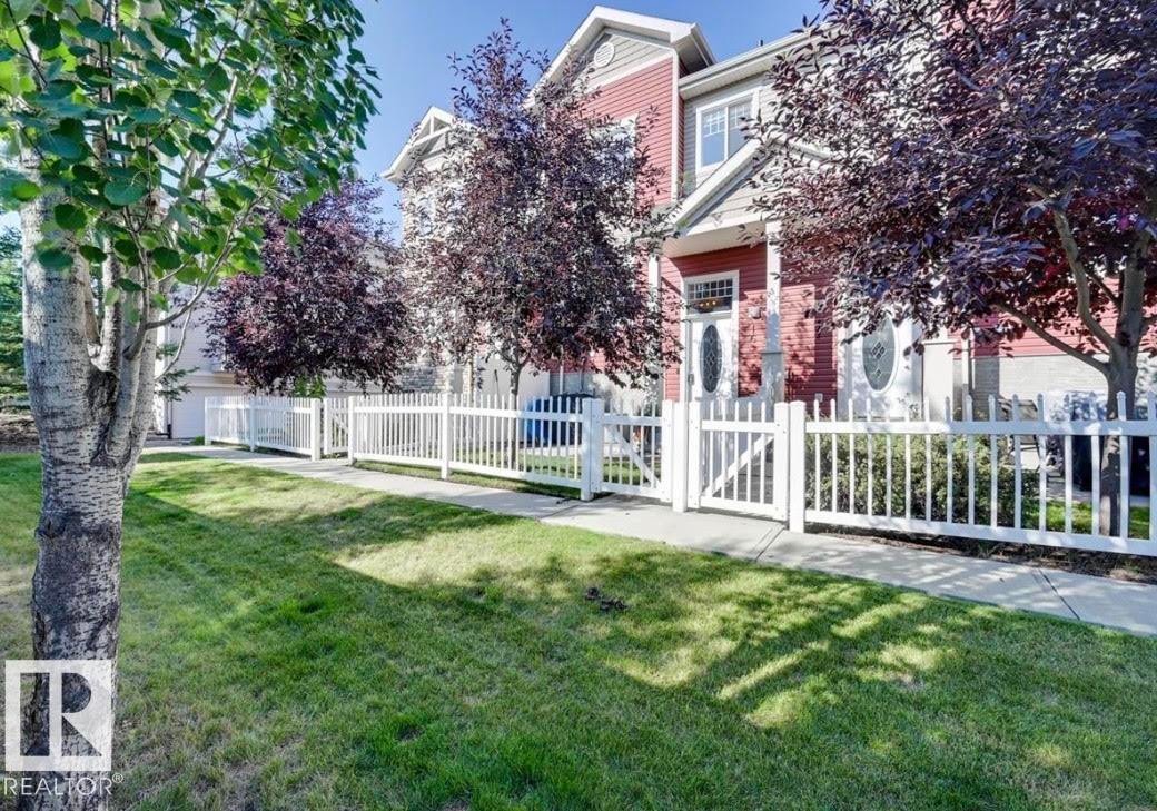 Red-sided townhouse with white trim, featuring a white picket fence and a manicured lawn - #16 460 Hemingway Rd Nw, Edmonton, AB - Outdoor
