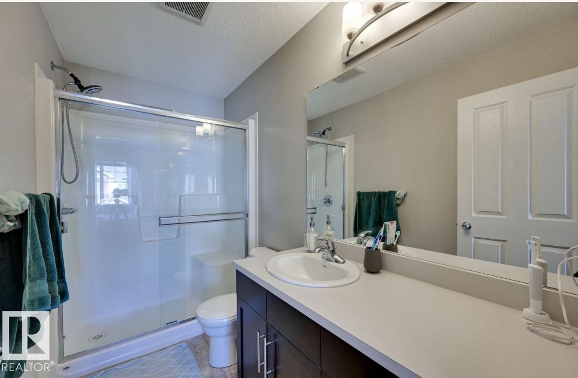 Bathroom featuring a dark wood-finish vanity with a single basin sink, white countertop, and expansive wall-mounted mirror - #16 460 Hemingway Rd Nw, Edmonton, AB - Indoor Photo Showing Bathroom
