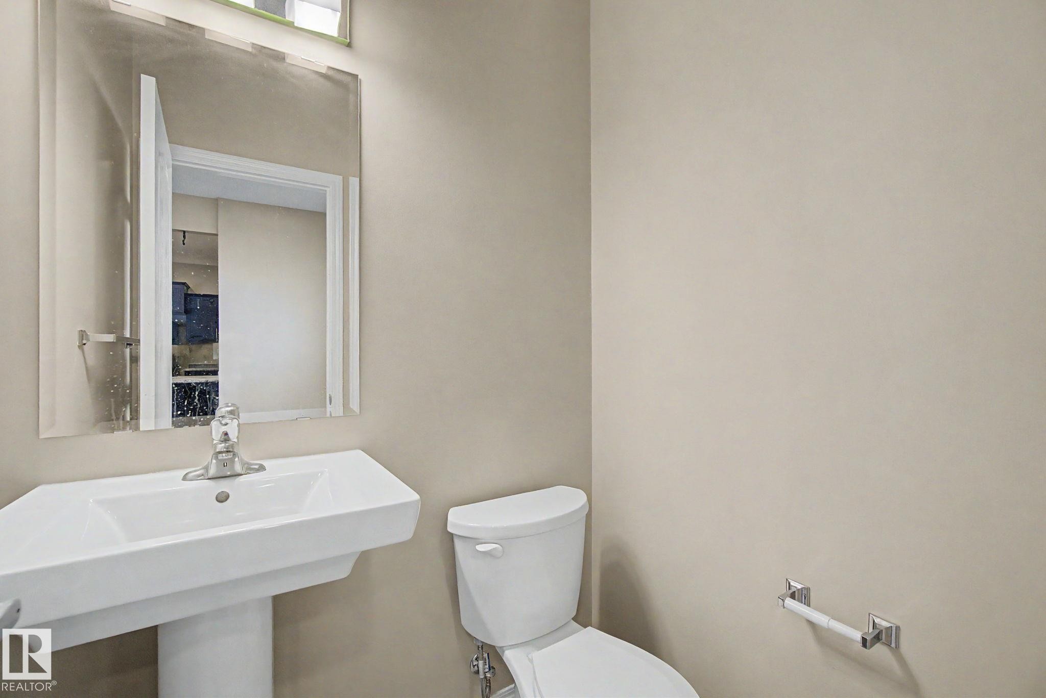 Pedestal sink with chrome faucet, wall-mounted mirror, white toilet, and neutral wall paint - 315 Watt Boulevard Sw, Edmonton, AB - Indoor Photo Showing Bathroom