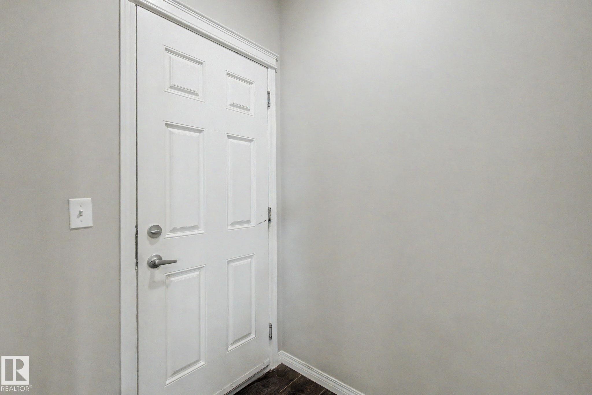 Six-panel interior door with brushed nickel hardware, light gray wall paint, white trim, and dark wood-finish flooring - 315 Watt Boulevard Sw, Edmonton, AB - Indoor Photo Showing Other Room