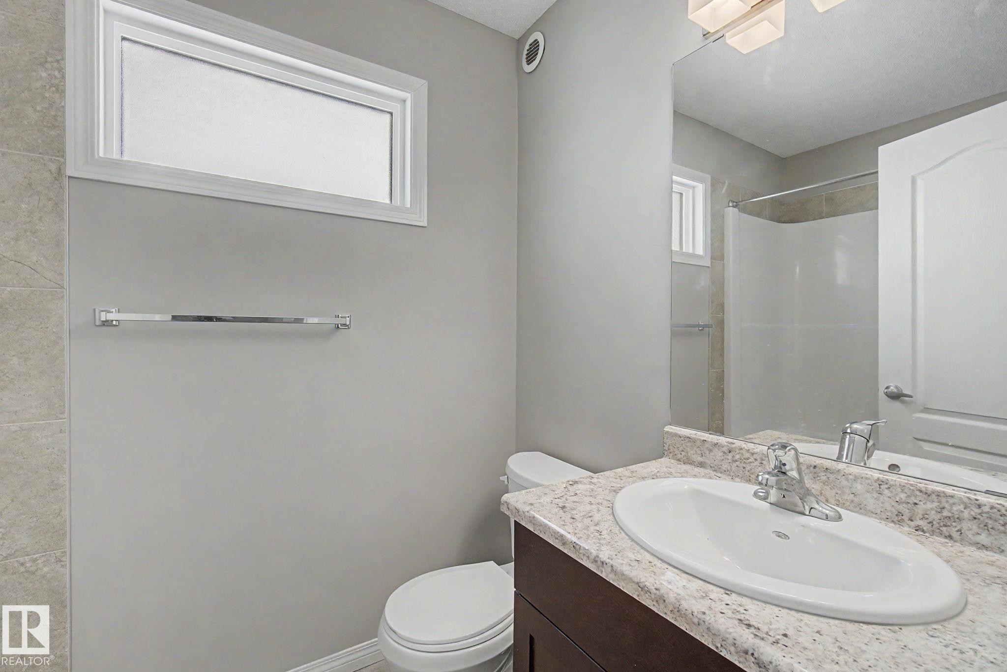 Bathroom featuring a dark wood-finish vanity with an undermount sink, a light speckled countertop, and a shower with tiled walls - 315 Watt Boulevard Sw, Edmonton, AB - Indoor Photo Showing Bathroom