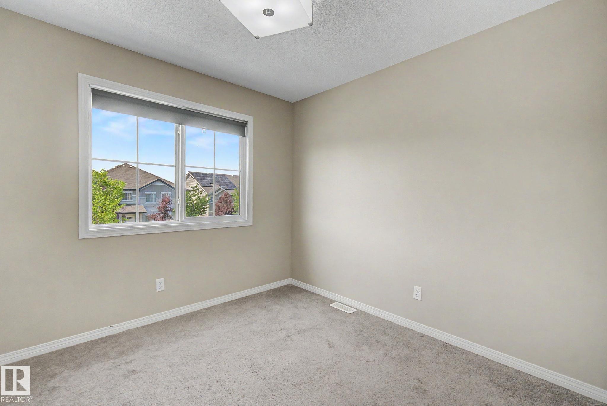 Bright room featuring a large window with white trim, light neutral wall paint, gray carpeting, and white baseboards - 315 Watt Boulevard Sw, Edmonton, AB - Indoor Photo Showing Other Room