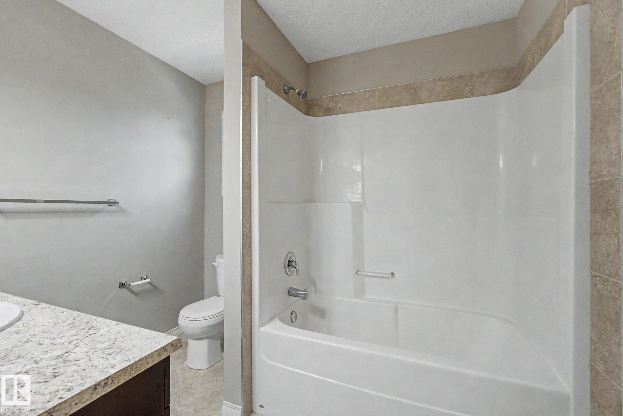 Full bath featuring a white tub/shower combination with integrated shelving, chrome fixtures, and tan tile surround - 315 Watt Boulevard Sw, Edmonton, AB - Indoor Photo Showing Bathroom