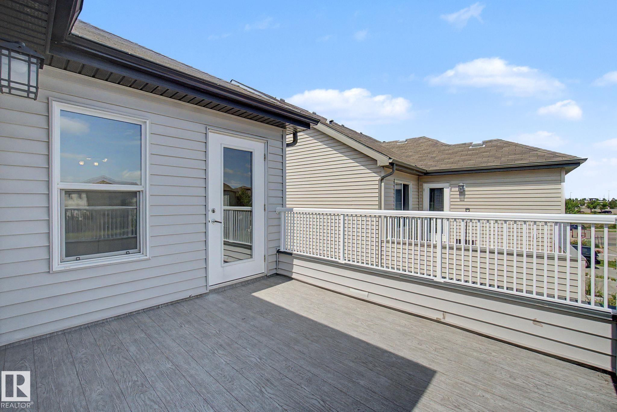 Spacious outdoor deck featuring wood-finish composite decking, white railing, and a glass-paneled door - 315 Watt Boulevard Sw, Edmonton, AB - Outdoor With Deck Patio Veranda With Exterior