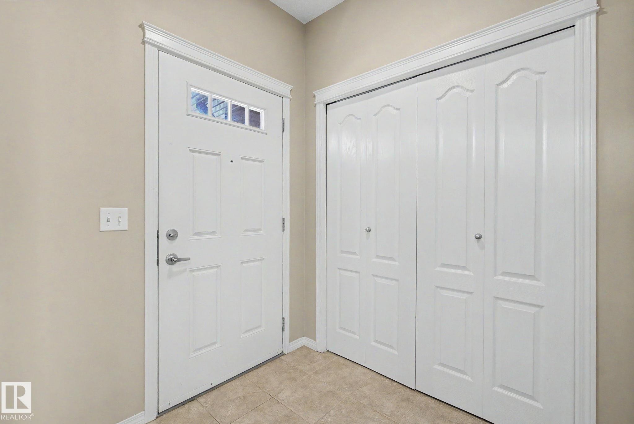 Entryway featuring a paneled door with decorative glass inserts, brushed nickel hardware, crown molding, a built-in closet with bifold doors, and neutral-toned tile flooring - 315 Watt Boulevard Sw, Edmonton, AB - Indoor Photo Showing Other Room
