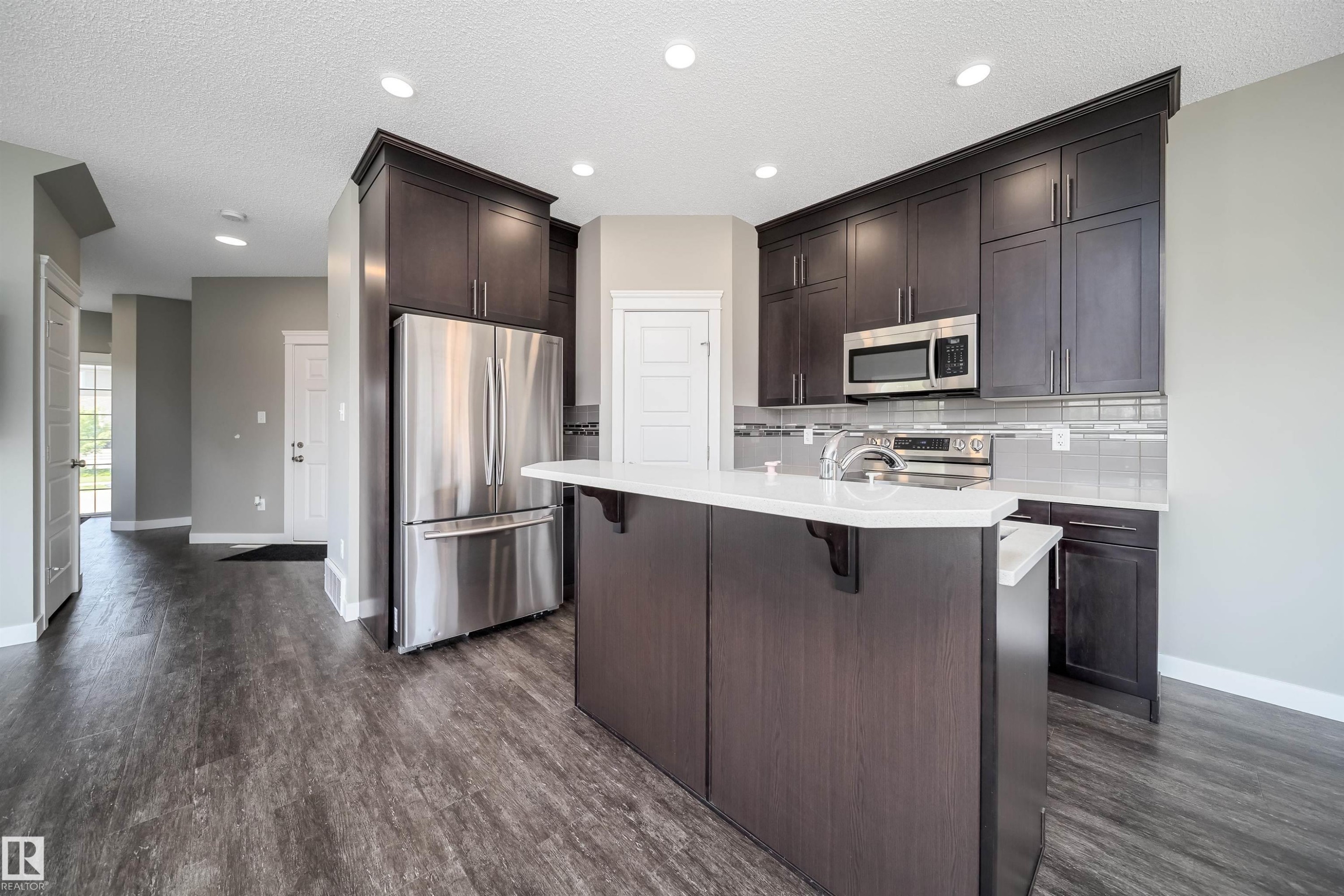 Kitchen featuring dark wood-finish cabinetry, stainless steel appliances, a center island with white countertop, and wood-finish flooring - 114 James Crescent, St. Albert, AB - Indoor Photo Showing Kitchen With Upgraded Kitchen