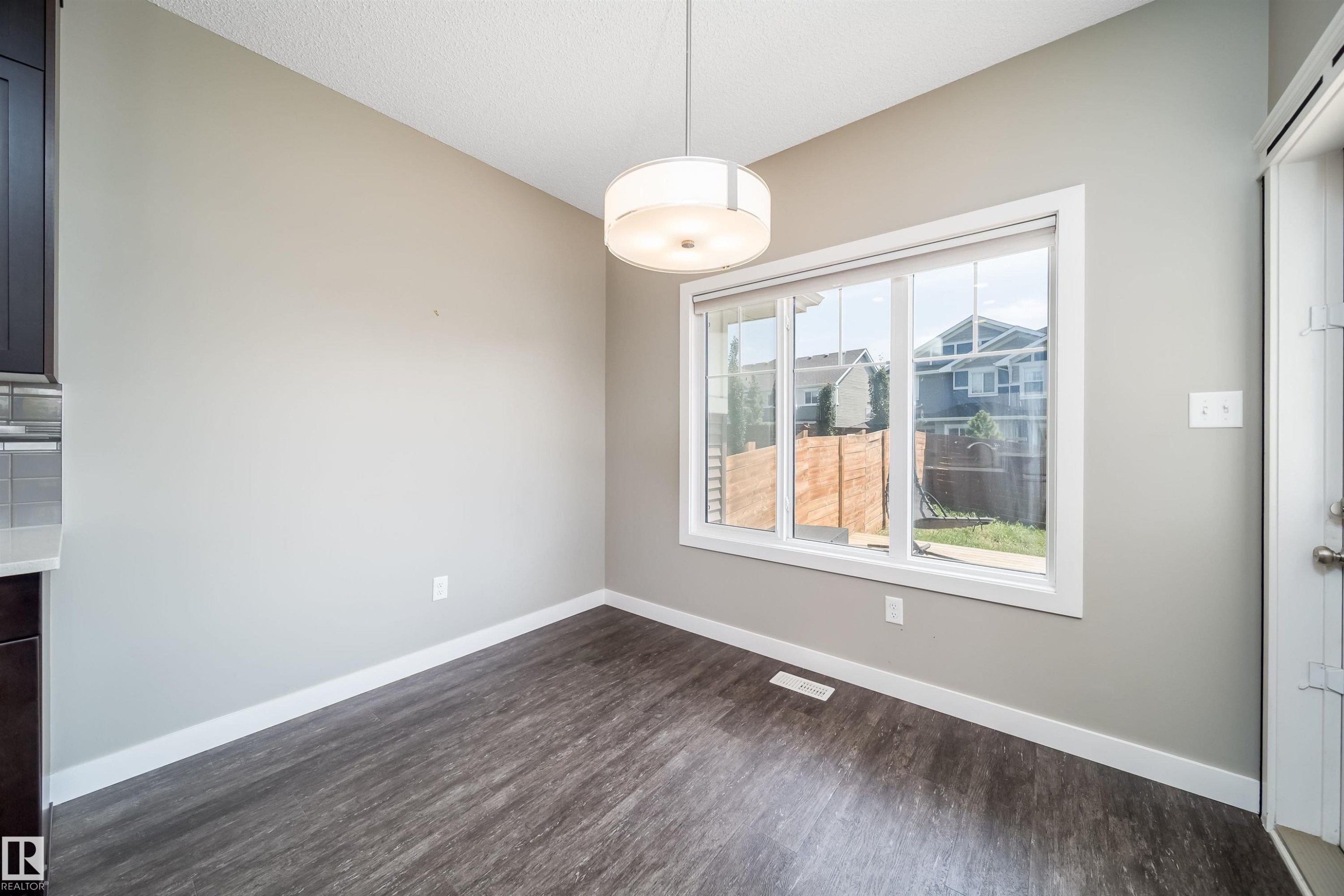 Bright dining space featuring a contemporary ceiling fixture, large window, wood-finish flooring, and light gray walls - 114 James Crescent, St. Albert, AB - Indoor Photo Showing Other Room